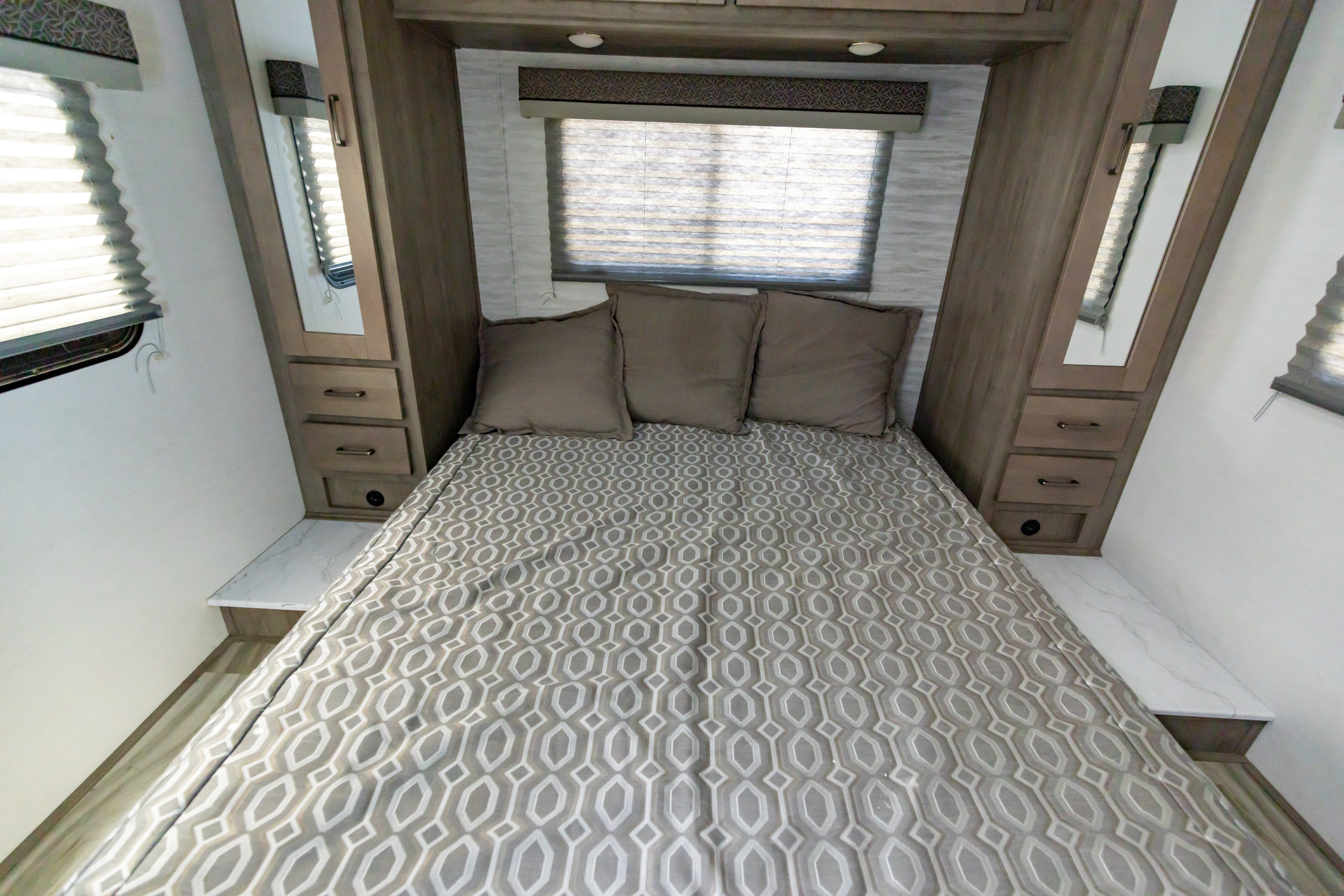 This RV rental bedroom features a comfy bed with a modern patterned comforter, window with blinds, and built-in storage.. Gulf Stream Conquest 2024