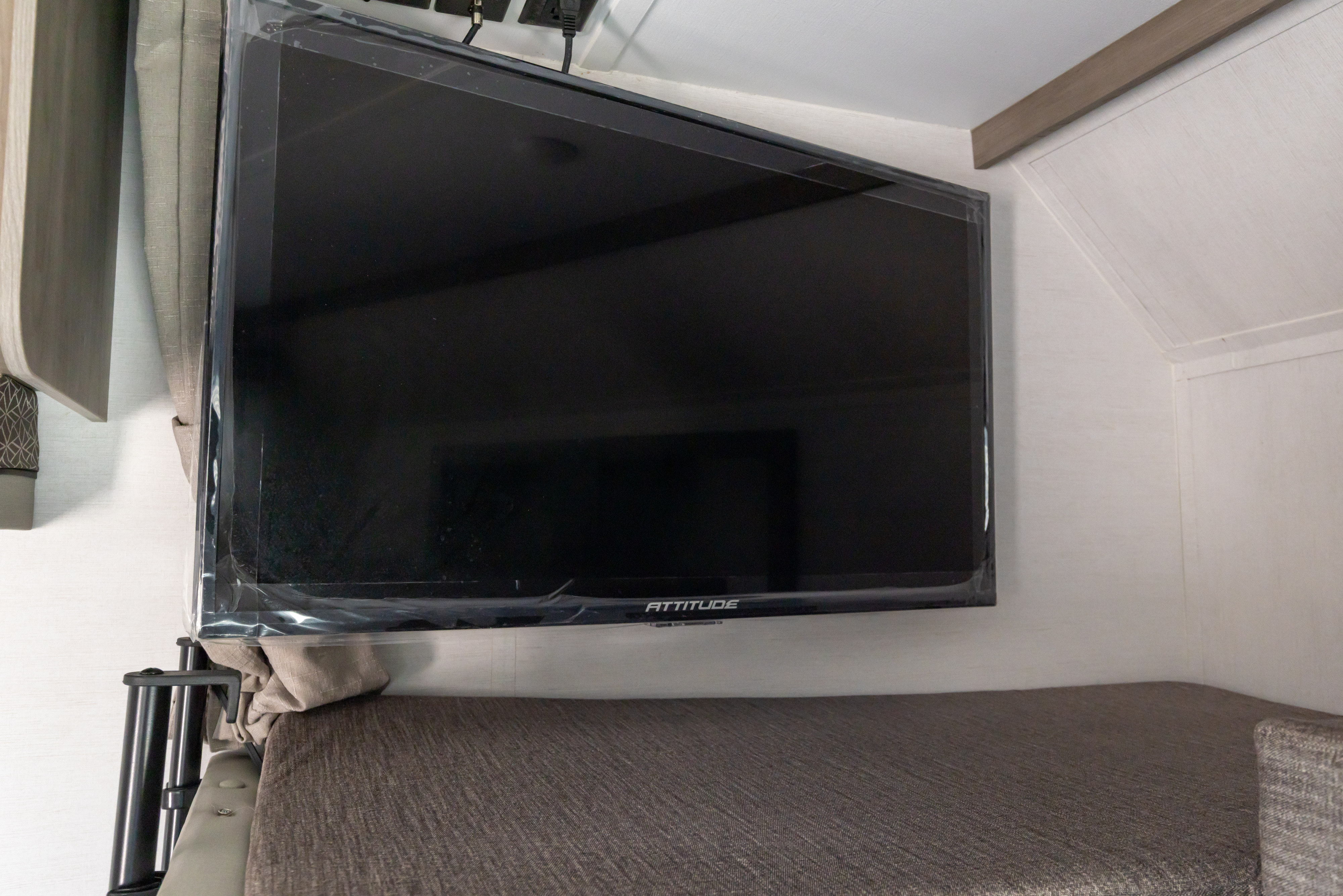 RV rental interior featuring a wall-mounted TV with protective film above a cushioned bunk bed or seating area.. Gulf Stream Conquest 2024