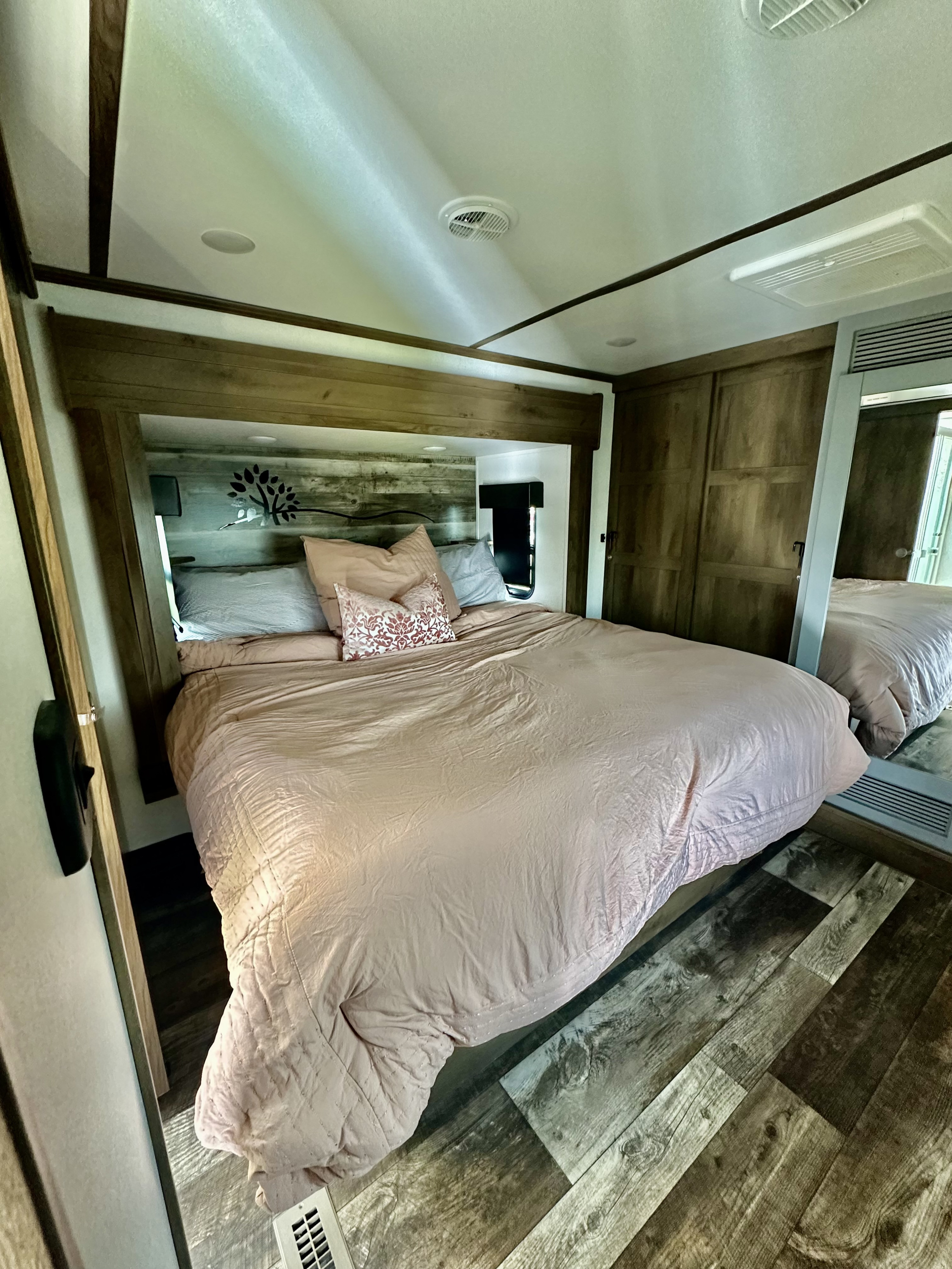 Spacious RV rental bedroom with a large bed, wood-paneled headboard, and mirrored closet. Perfect for travel.. Keystone RV Fuzion Toy Hauler 2021