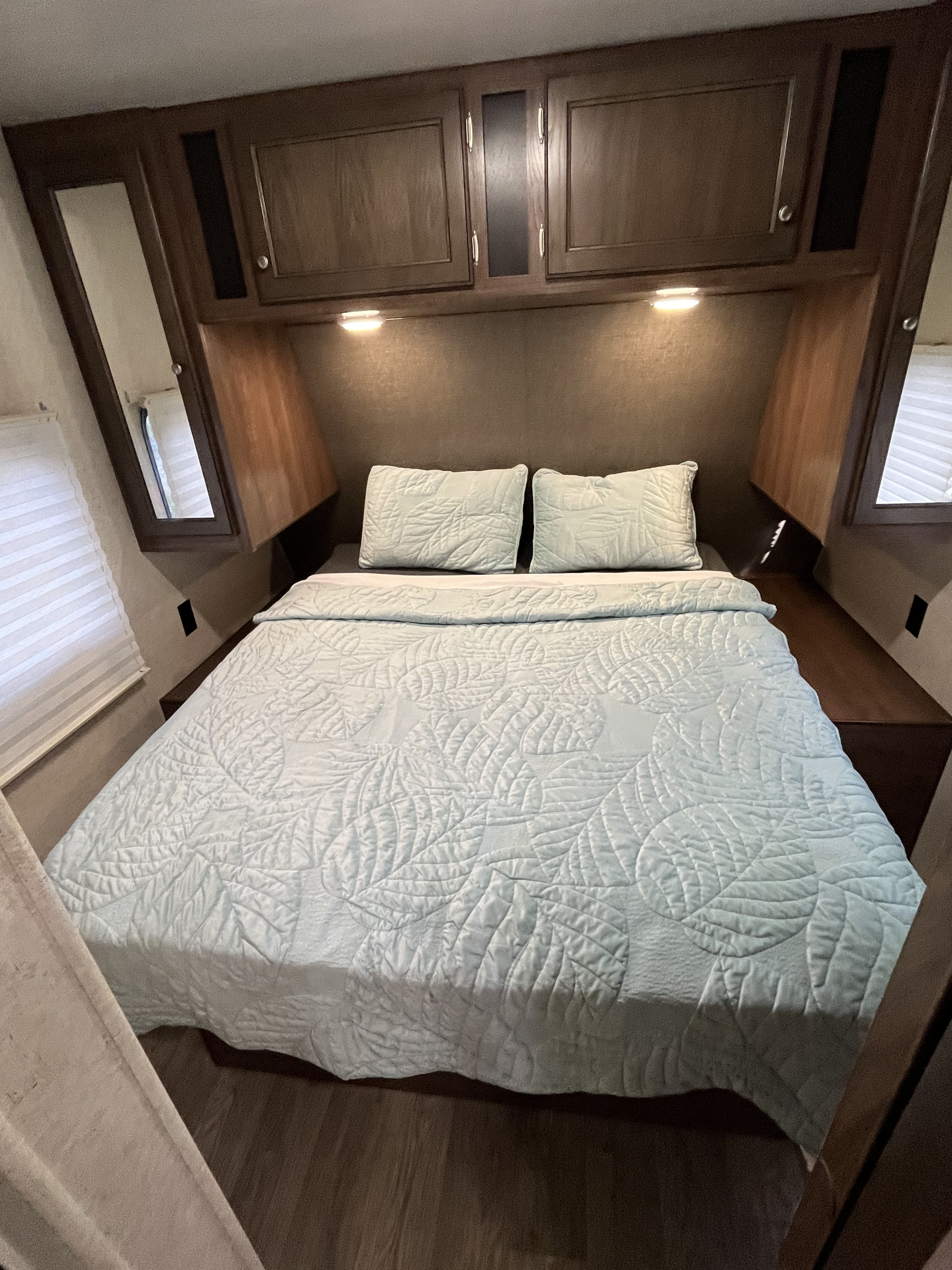 This inviting RV rental bedroom features a light blue quilted bed, overhead storage, and ambient lighting, maximizing comfort in a compact space.. Heartland Prowler 2019