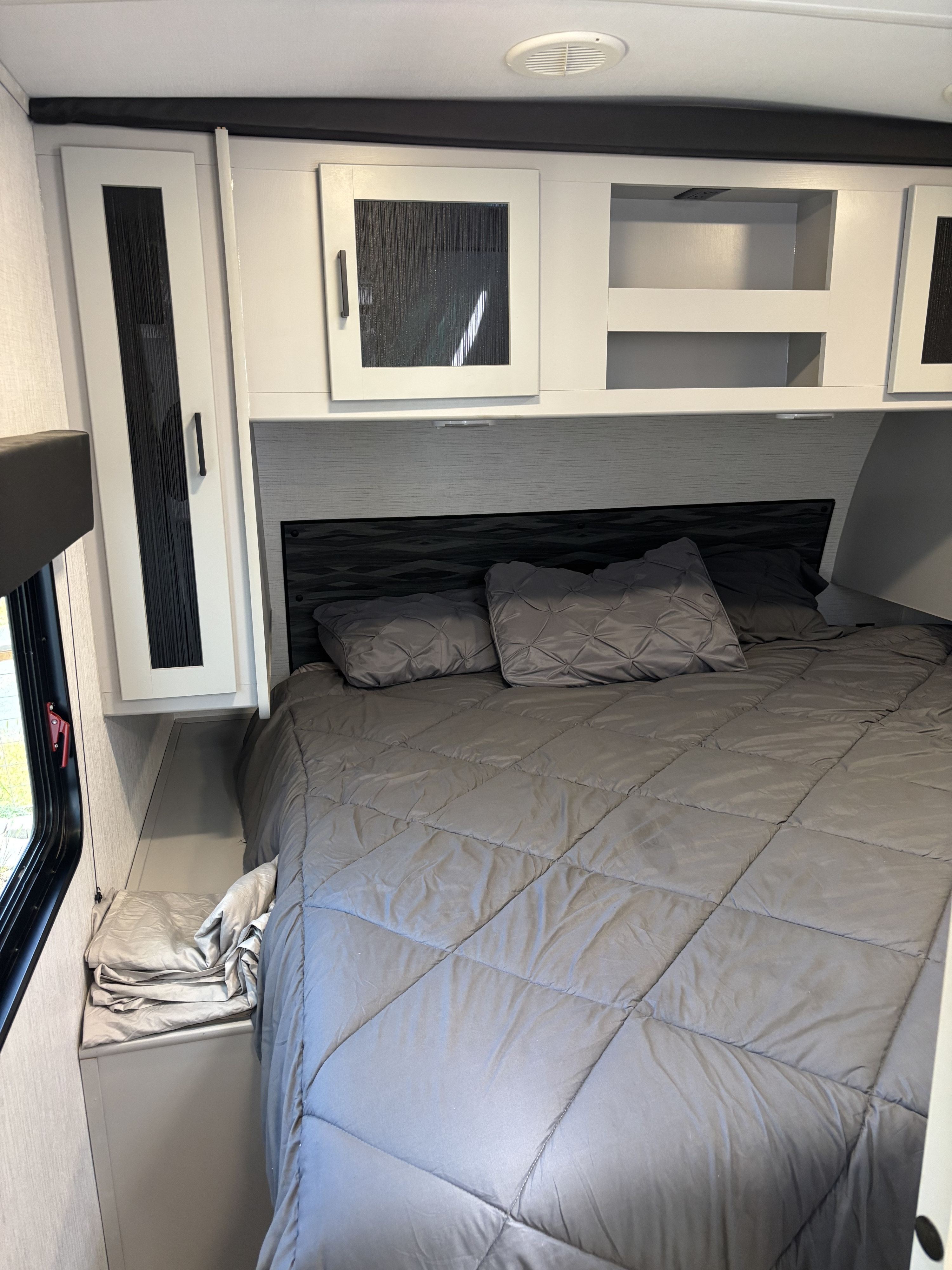 Cozy RV rental bedroom with grey bed, textured headboard, and white overhead cabinets for ample storage.. Heartland RVs North Trail 2022