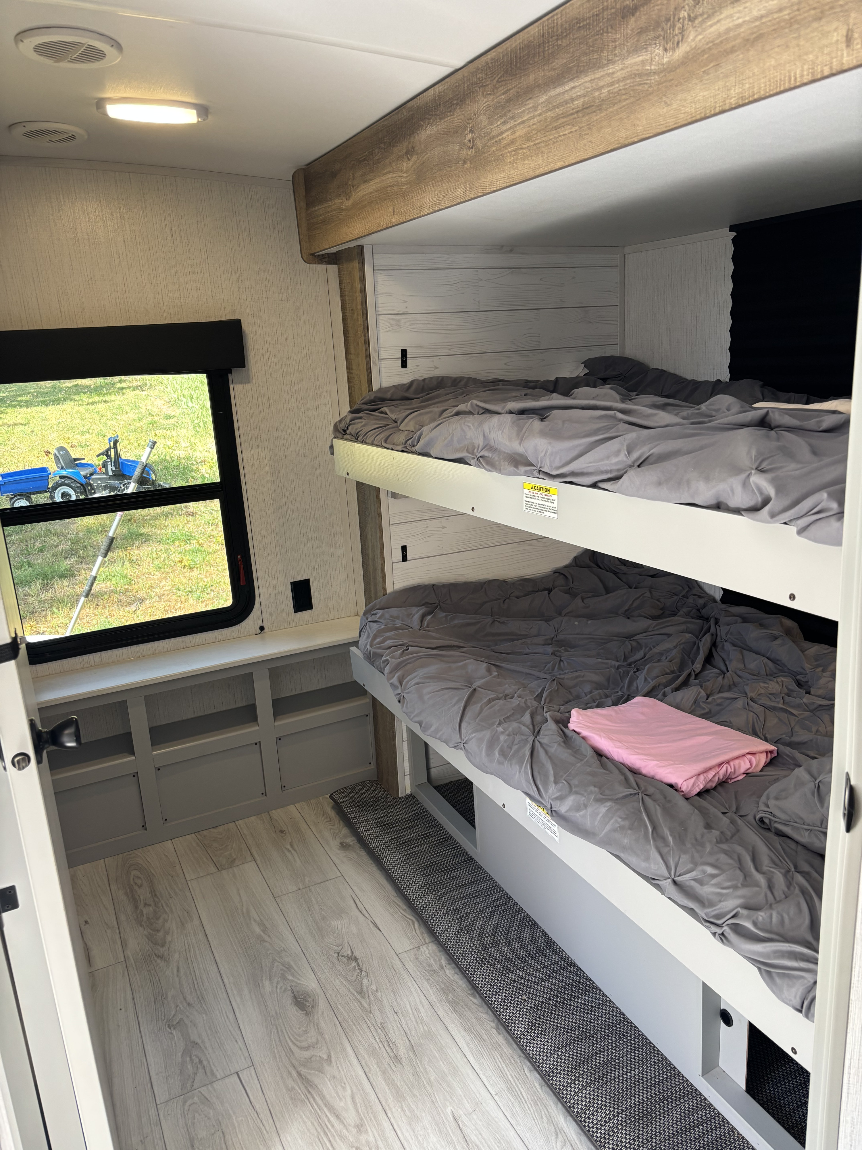 Cozy bunk beds in an RV rental, with light wood flooring, a window view, and built-in storage. Ideal for family travel.. Heartland RVs North Trail 2022