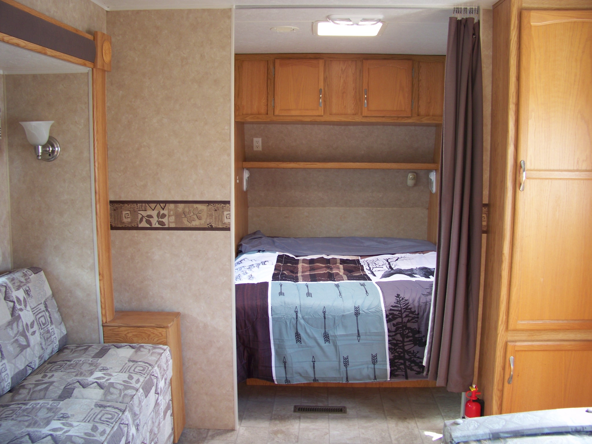 RV rental bedroom area with a patterned comforter, overhead cabinets, pull-out curtain, and an adjacent sofa.. Holiday Rambler Savoy LE 2007