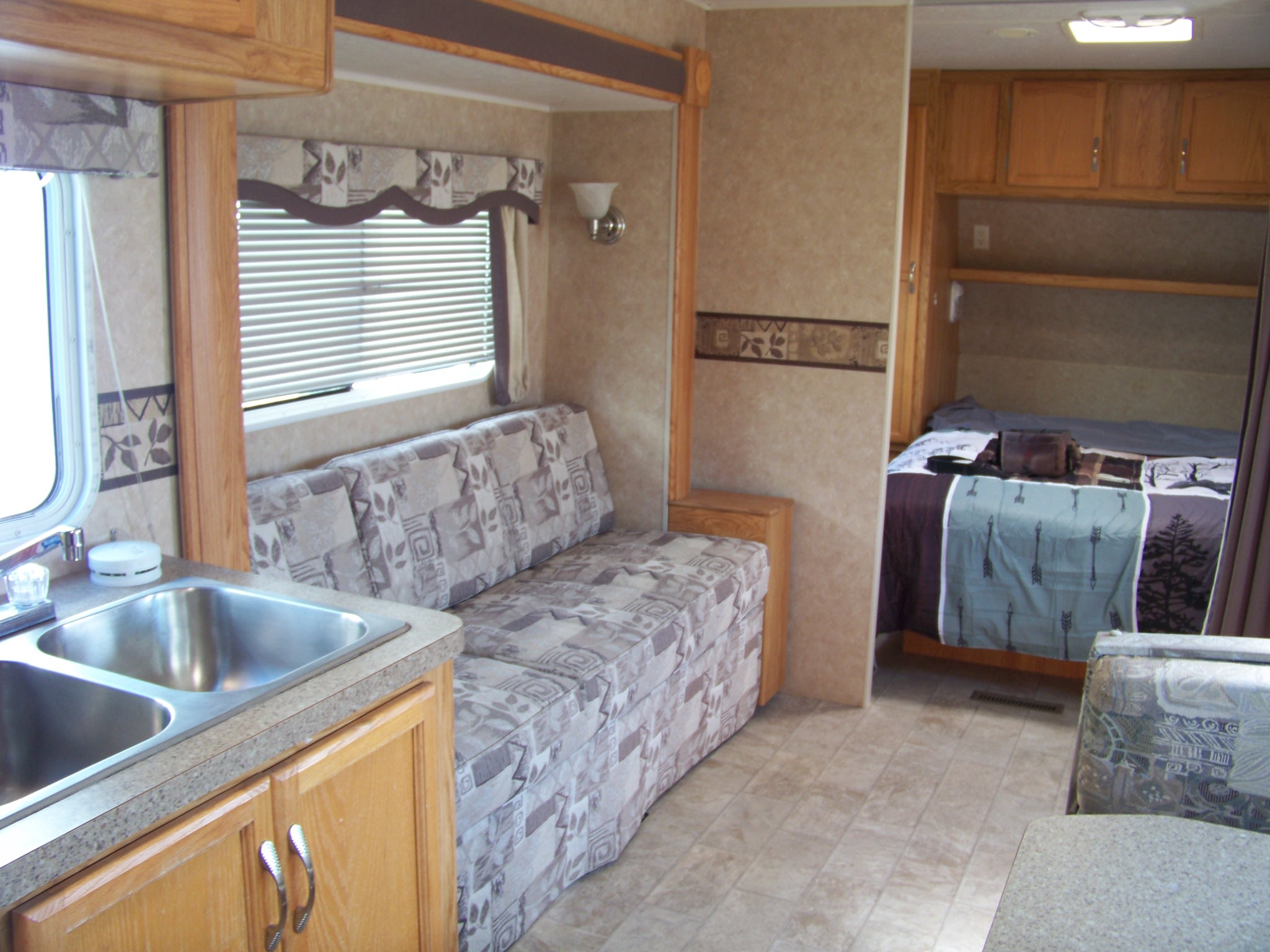 View of a clean RV rental interior, showcasing a double sink kitchen, patterned sofa living area, and a cozy bedroom. Ready for travel.. Holiday Rambler Savoy LE 2007