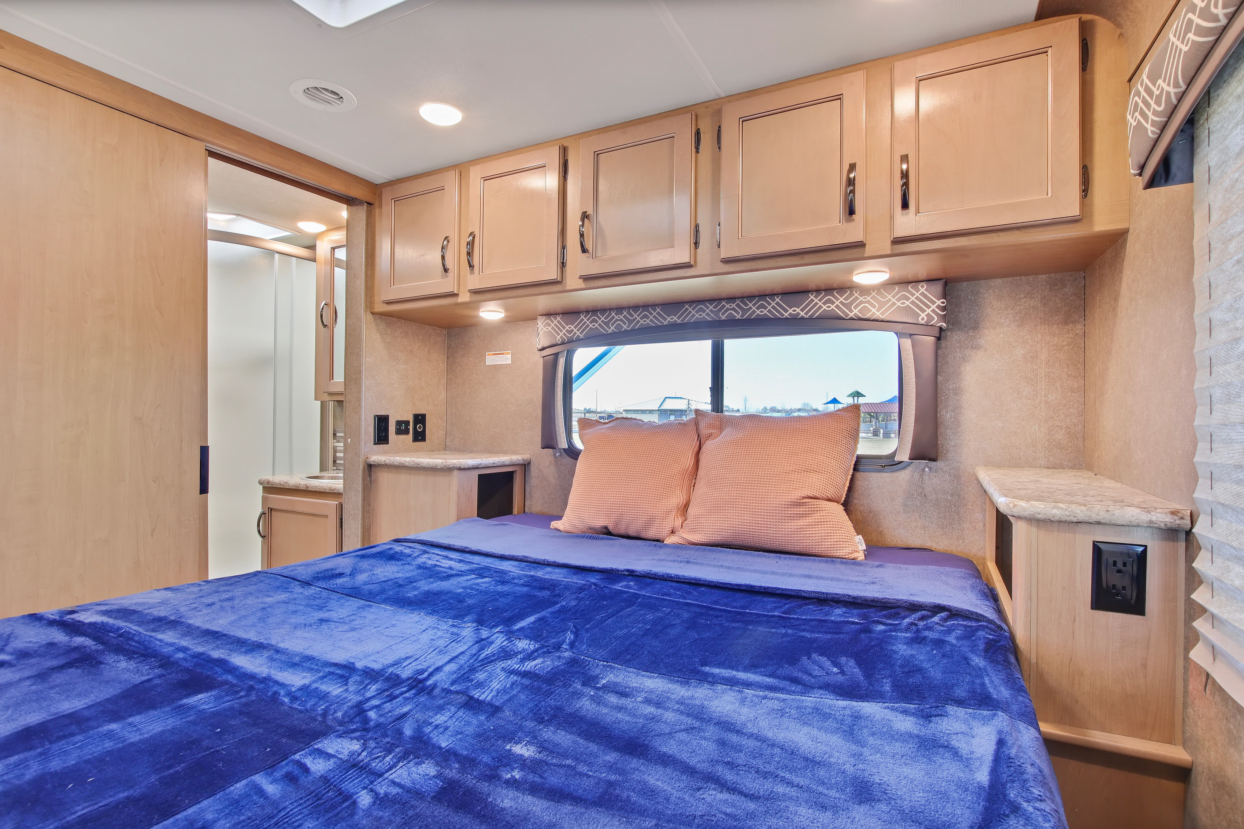 This RV rental bedroom features a cozy bed with blue bedding, ample overhead cabinets, and a sliding door to the attached bathroom.. Thor Chateau 2020