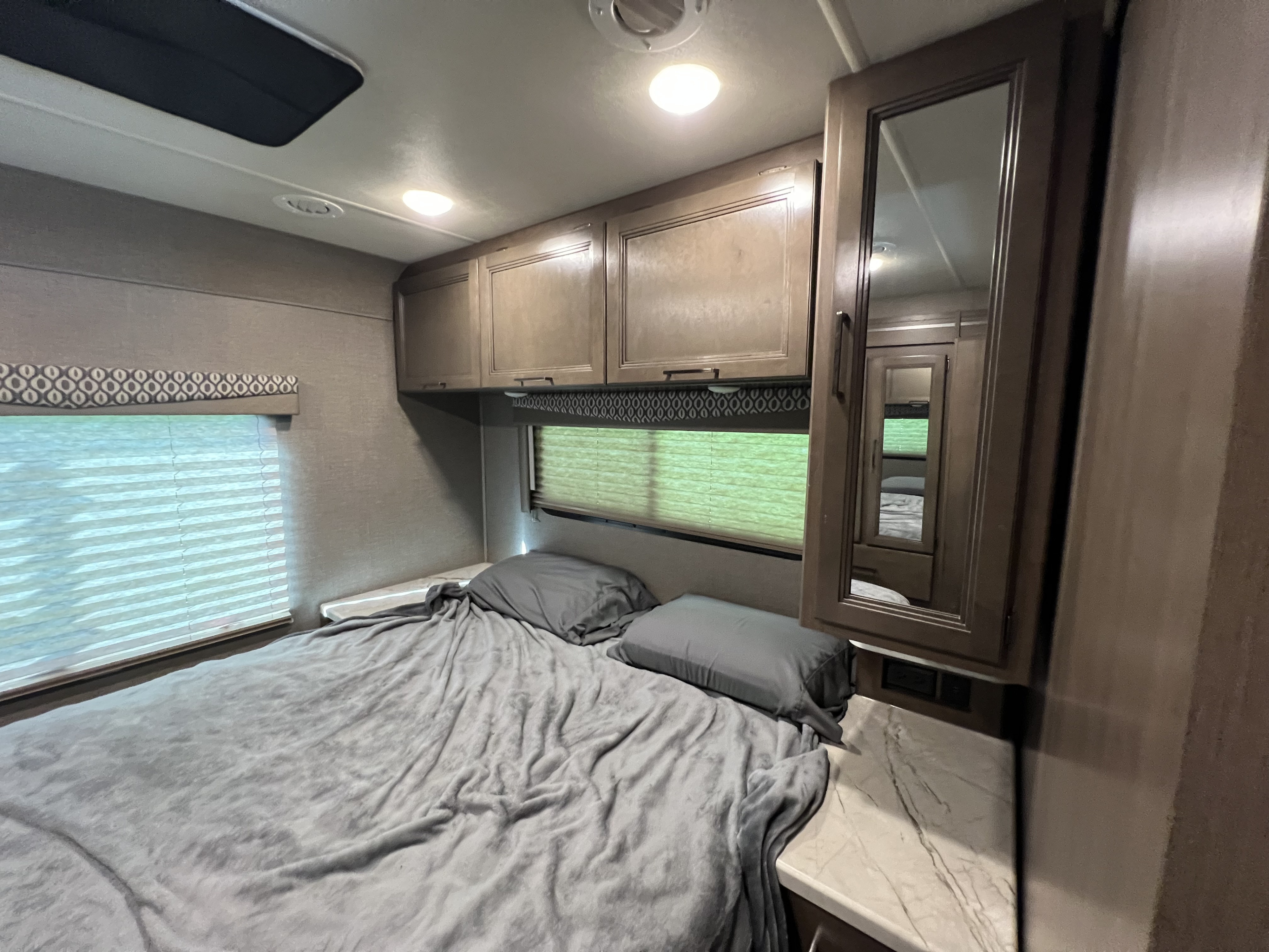 Inside an RV rental: A compact bedroom with gray bedding, an RV window, storage cabinets, and a mirrored wardrobe.. Thor Freedom Elite 2021