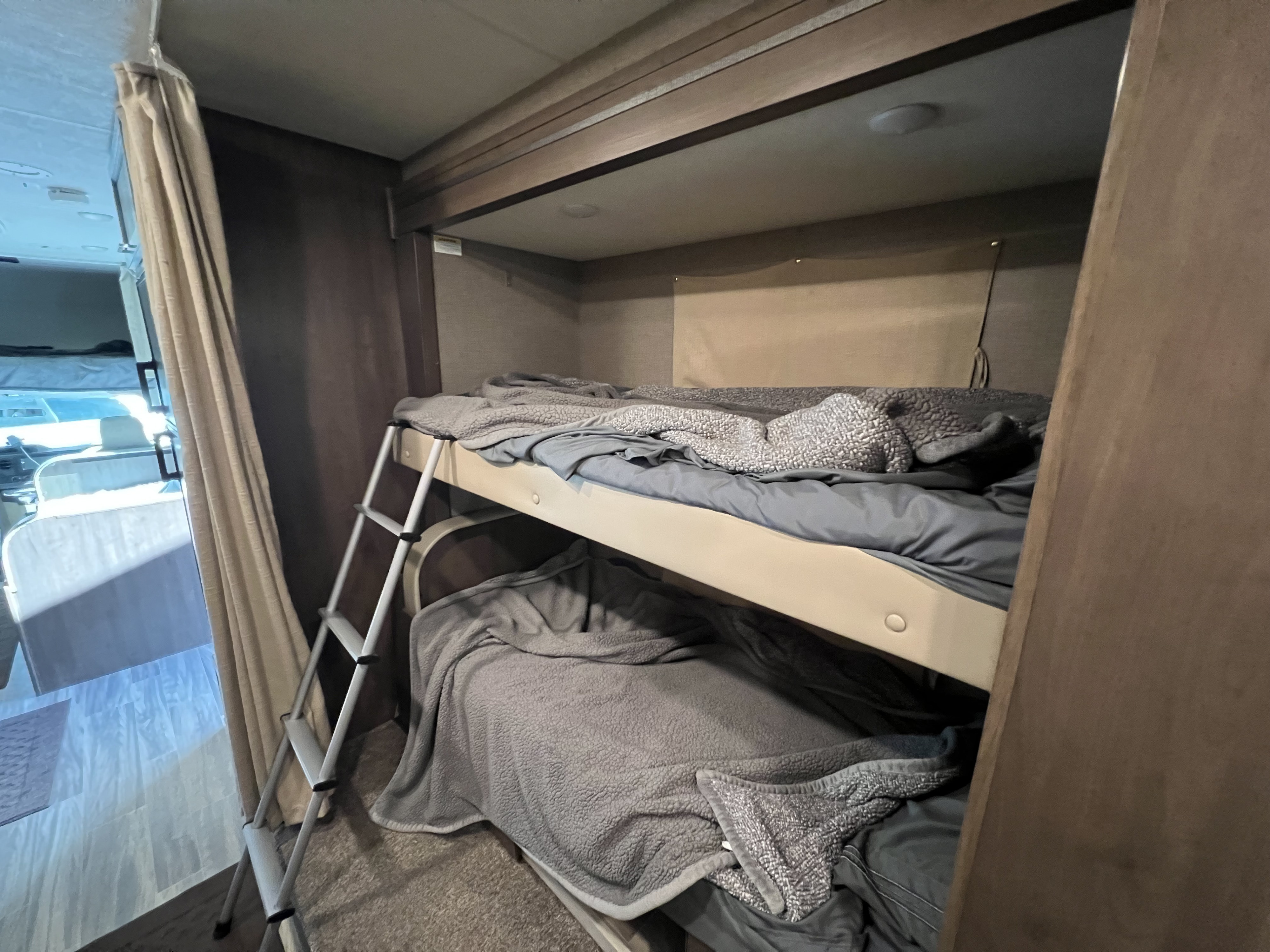View inside an RV rental showing stacked bunk beds with a metal ladder. Soft gray sheets and blankets make them look comfortable, great for sleeping on the go.. Thor Freedom Elite 2021