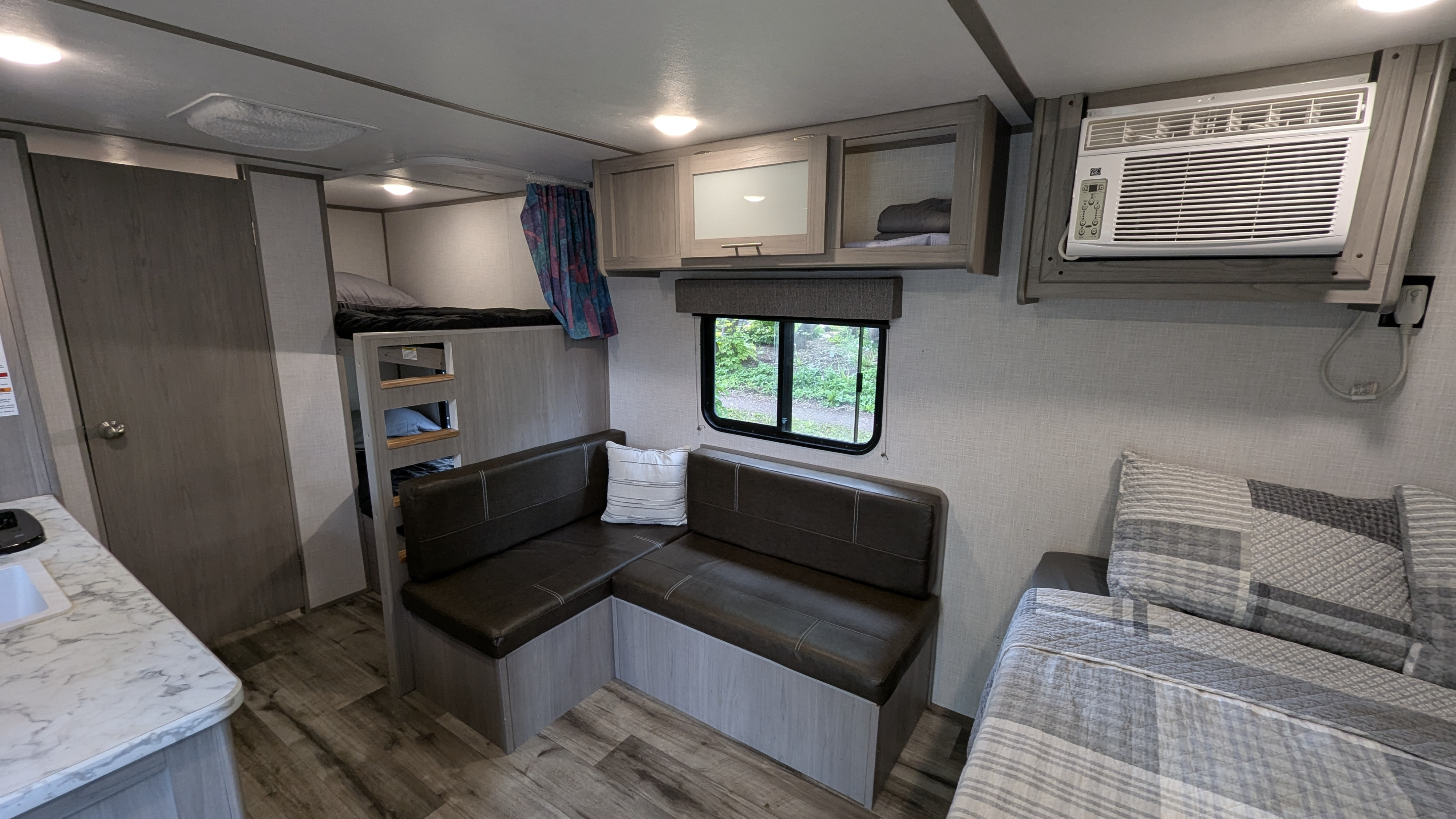 Inside an RV rental: includes bunk beds, an L-shaped dinette, kitchen counter, overhead cabinets, and AC.. Dutchmen Coleman Lantern LT 2022