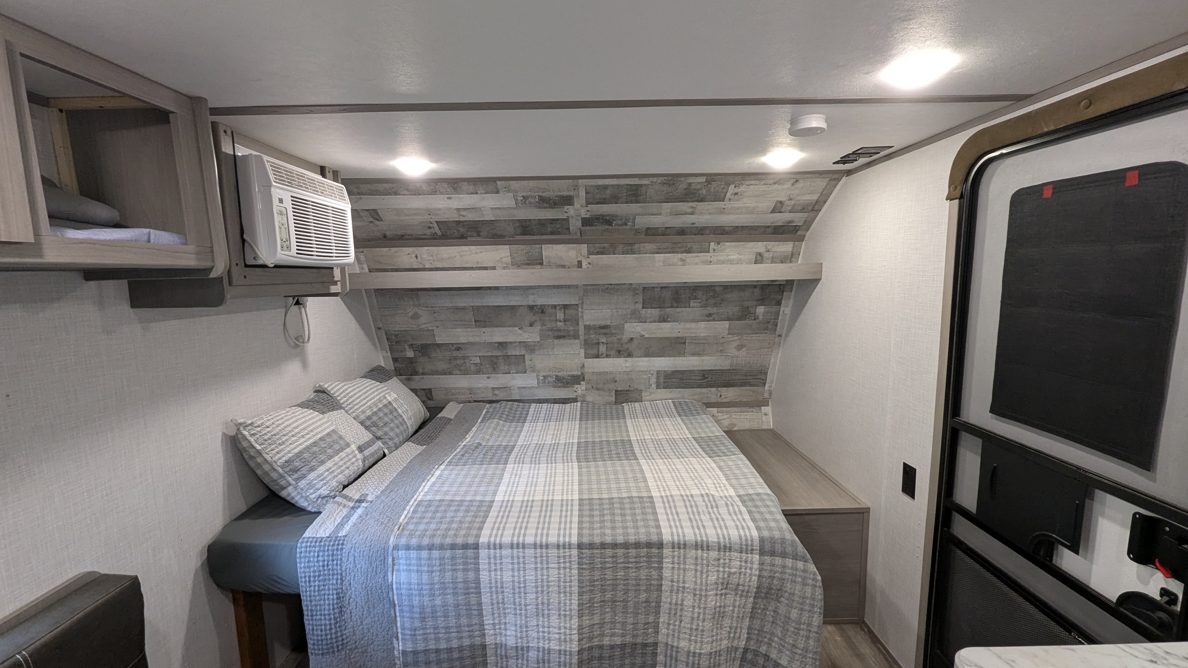 Cozy RV rental bedroom with a plaid bed, overhead AC, and rustic wood-paneled wall, designed for comfort on the go.. Dutchmen Coleman Lantern LT 2022