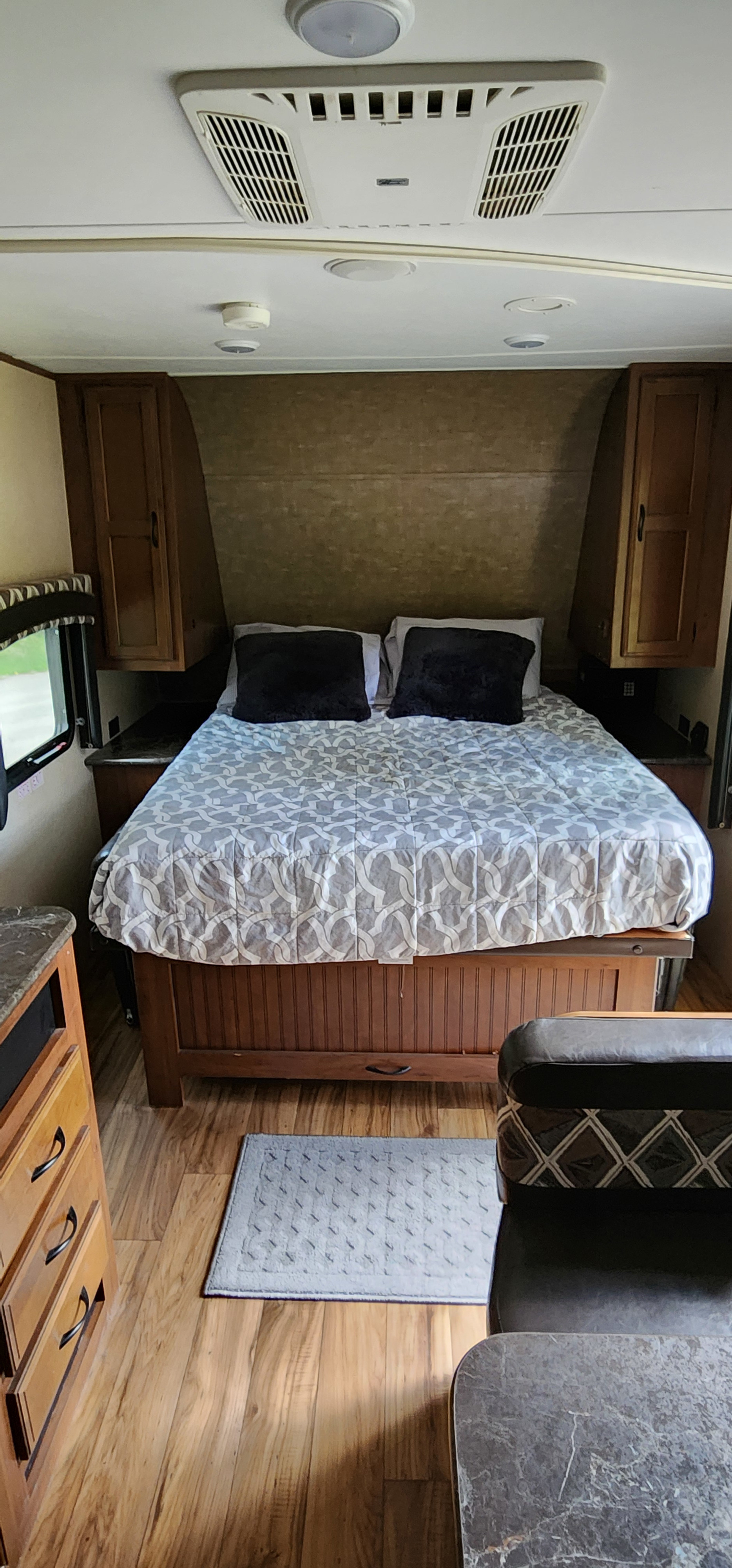 Inside this spacious RV rental: a comfortable bedroom with a patterned bed, wood accents, and ceiling AC.. Jayco 23MB 2016