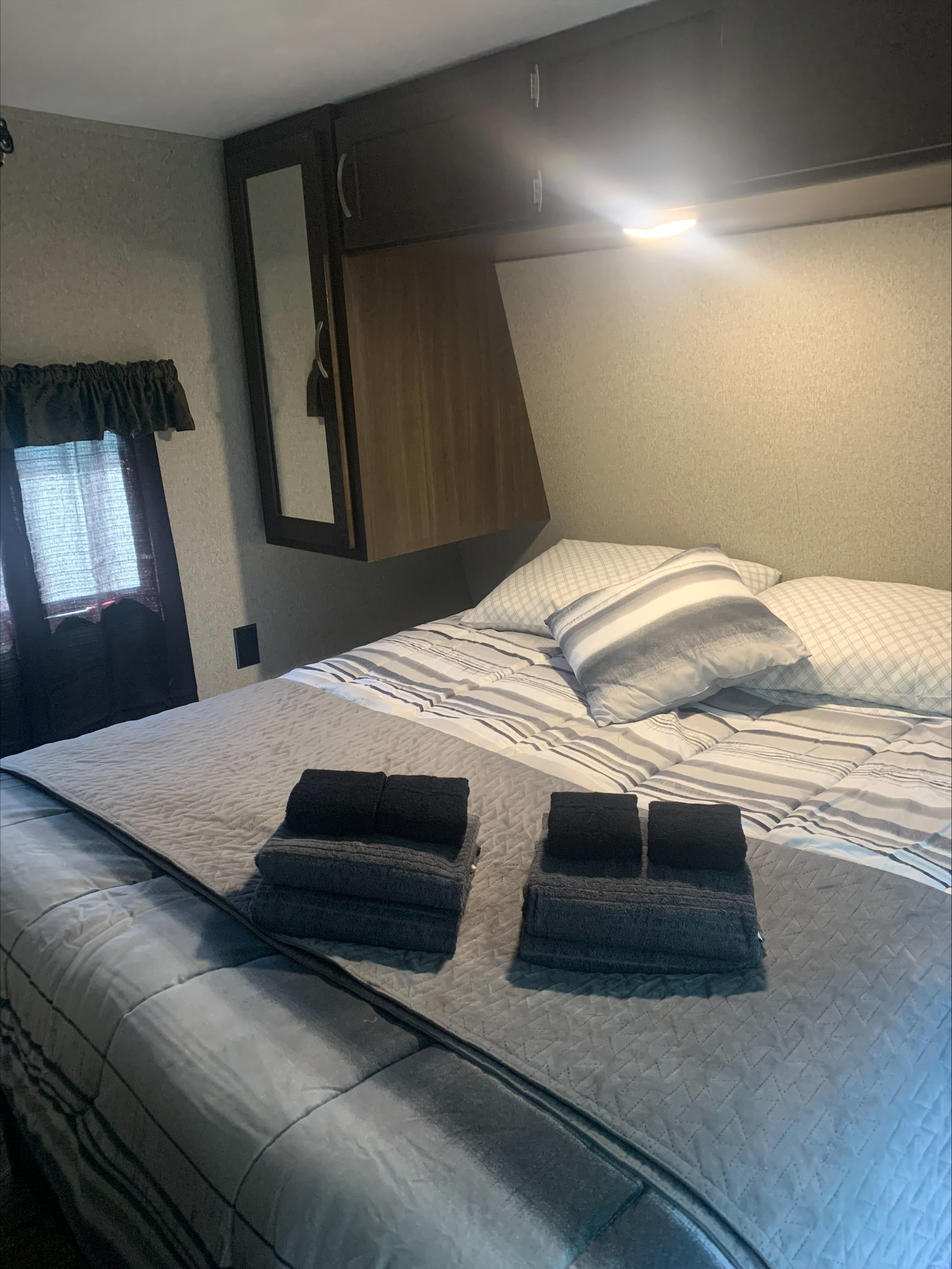 Cozy RV rental bedroom featuring a comfortable bed, fresh towels, overhead cabinets, and a window.. Keystone RV Springdale 2019