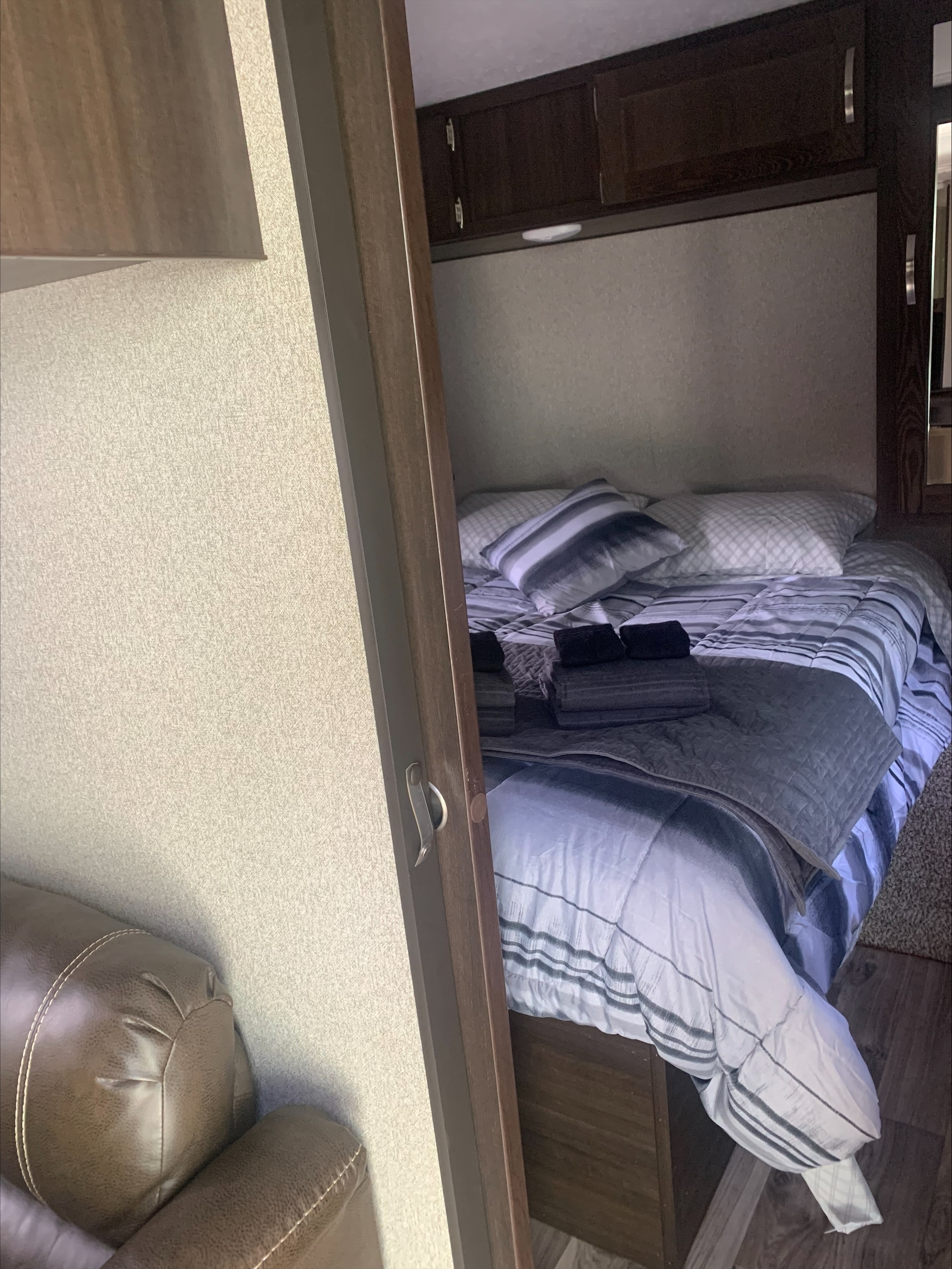 RV rental: A modern bedroom with striped bedding, pillows, and dark wood overhead cabinets.. Keystone RV Springdale 2019
