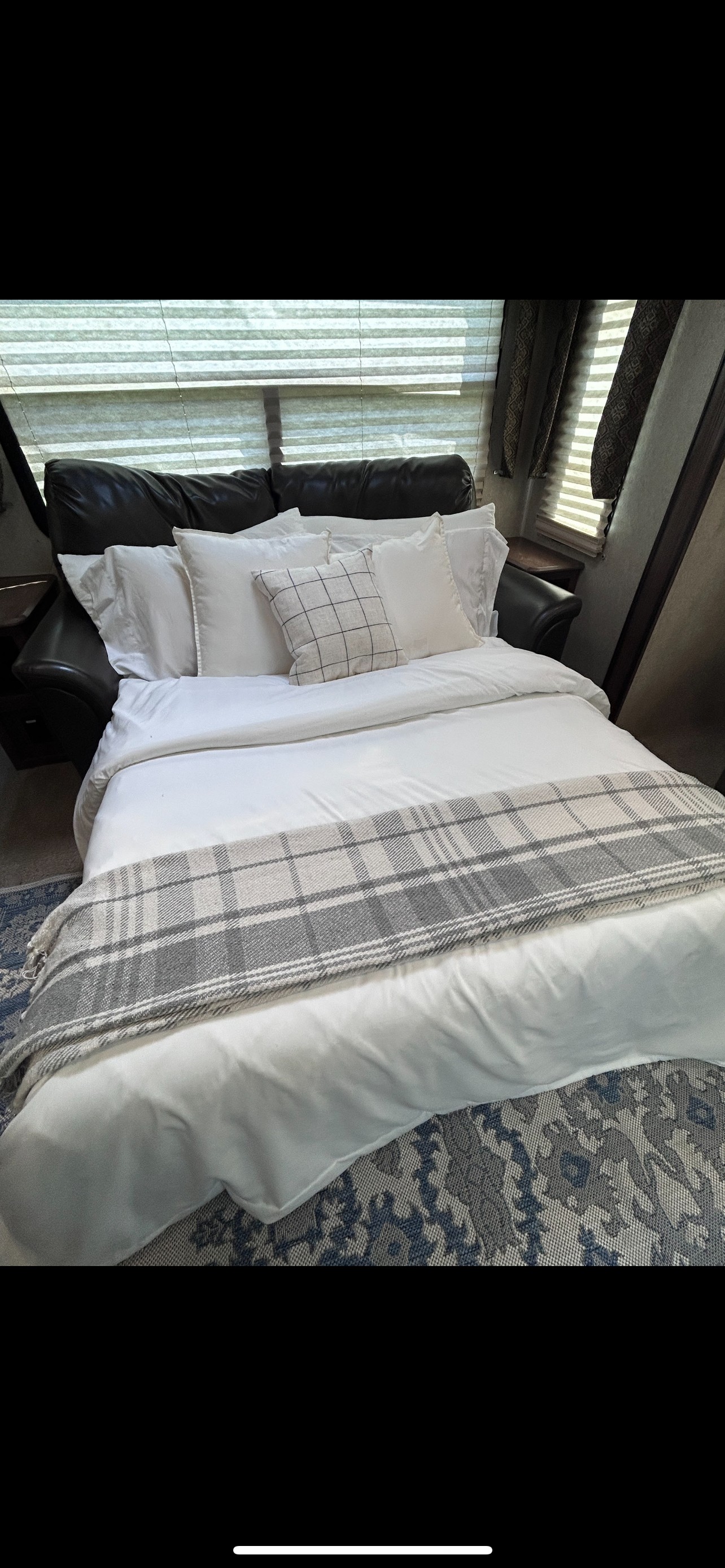 Comfortable sofa bed in an RV rental with white bedding, a plaid blanket, and a patterned rug.. Forest River Flagstaff V-Lite 2016