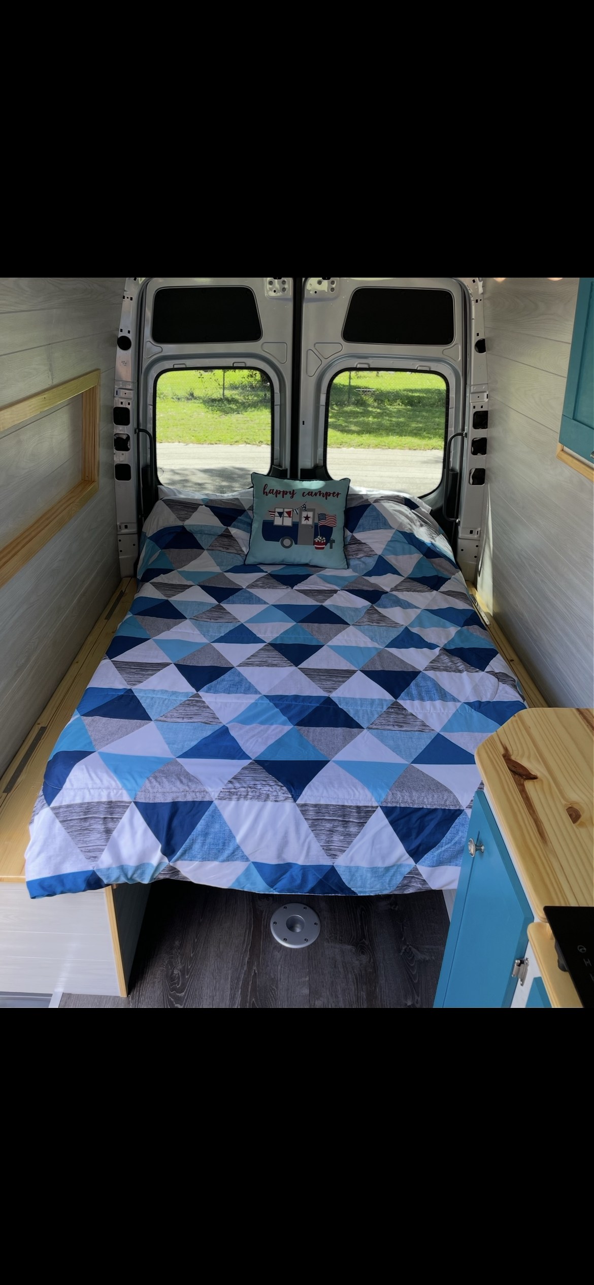 RV rental interior: Cozy camper van bedroom featuring a blue patterned bed & wood paneling. Perfect for adventures!. Mercedes-Benz Sprinter 2019