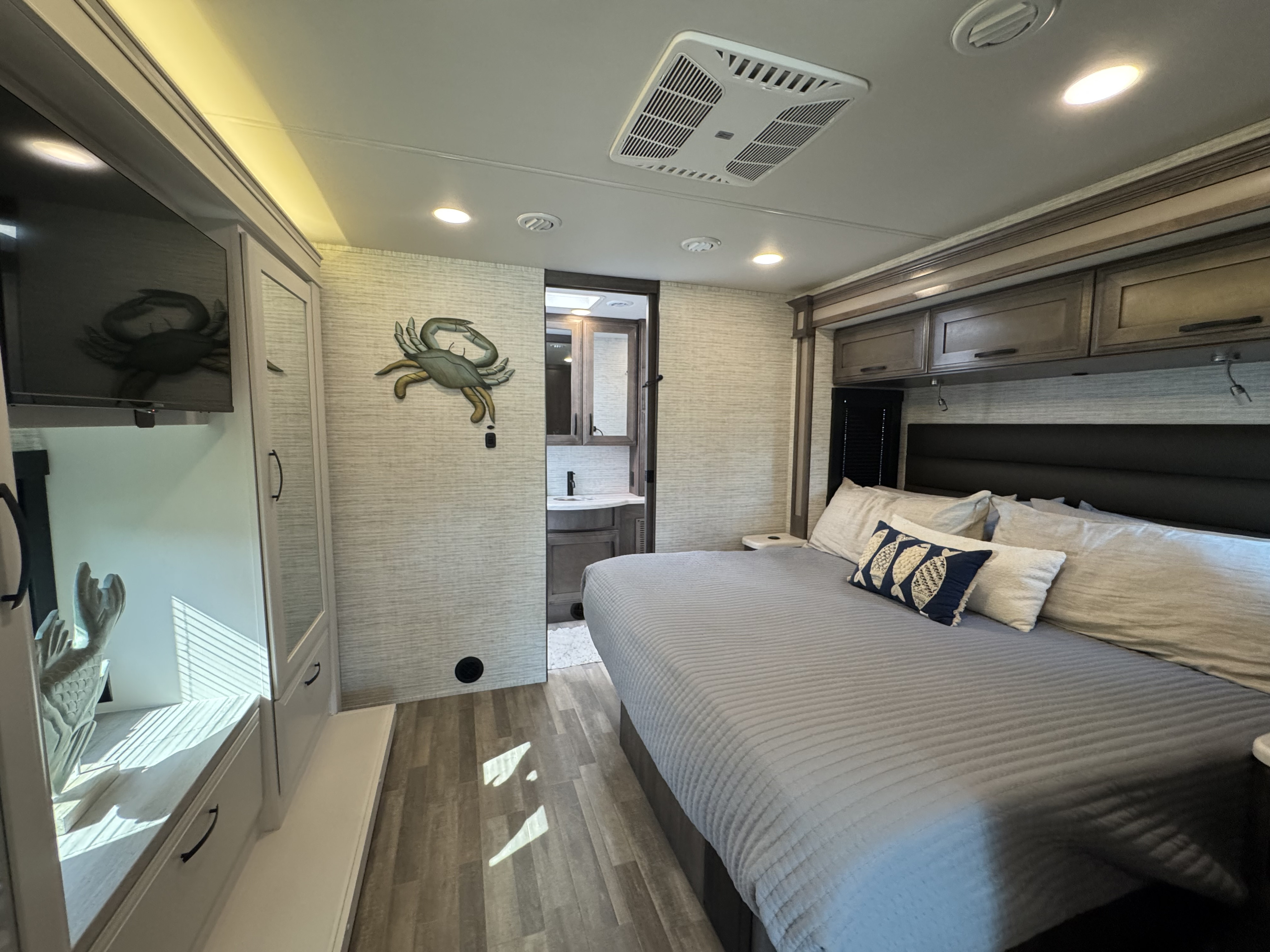 Spacious RV rental bedroom featuring a comfy bed, TV, crab decor, and en-suite bath access.. Entegra Vision XL 36C 2025