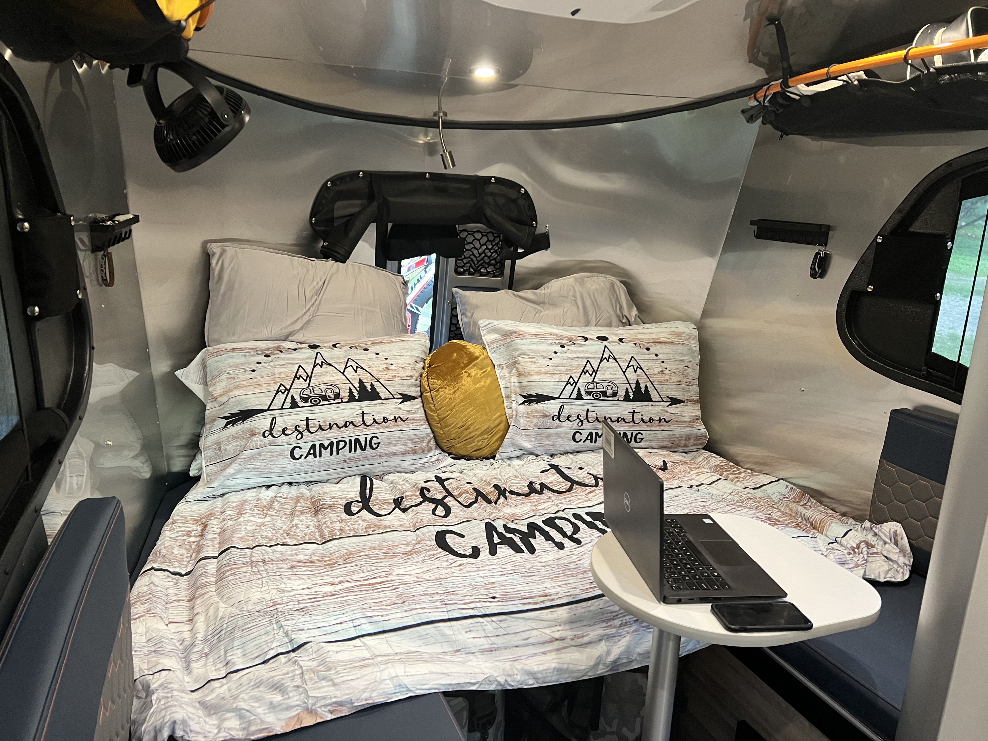 Cozy RV rental interior featuring a 'Destination Camping' bed, laptop table, and integrated amenities.. Airstream Basecamp 2022