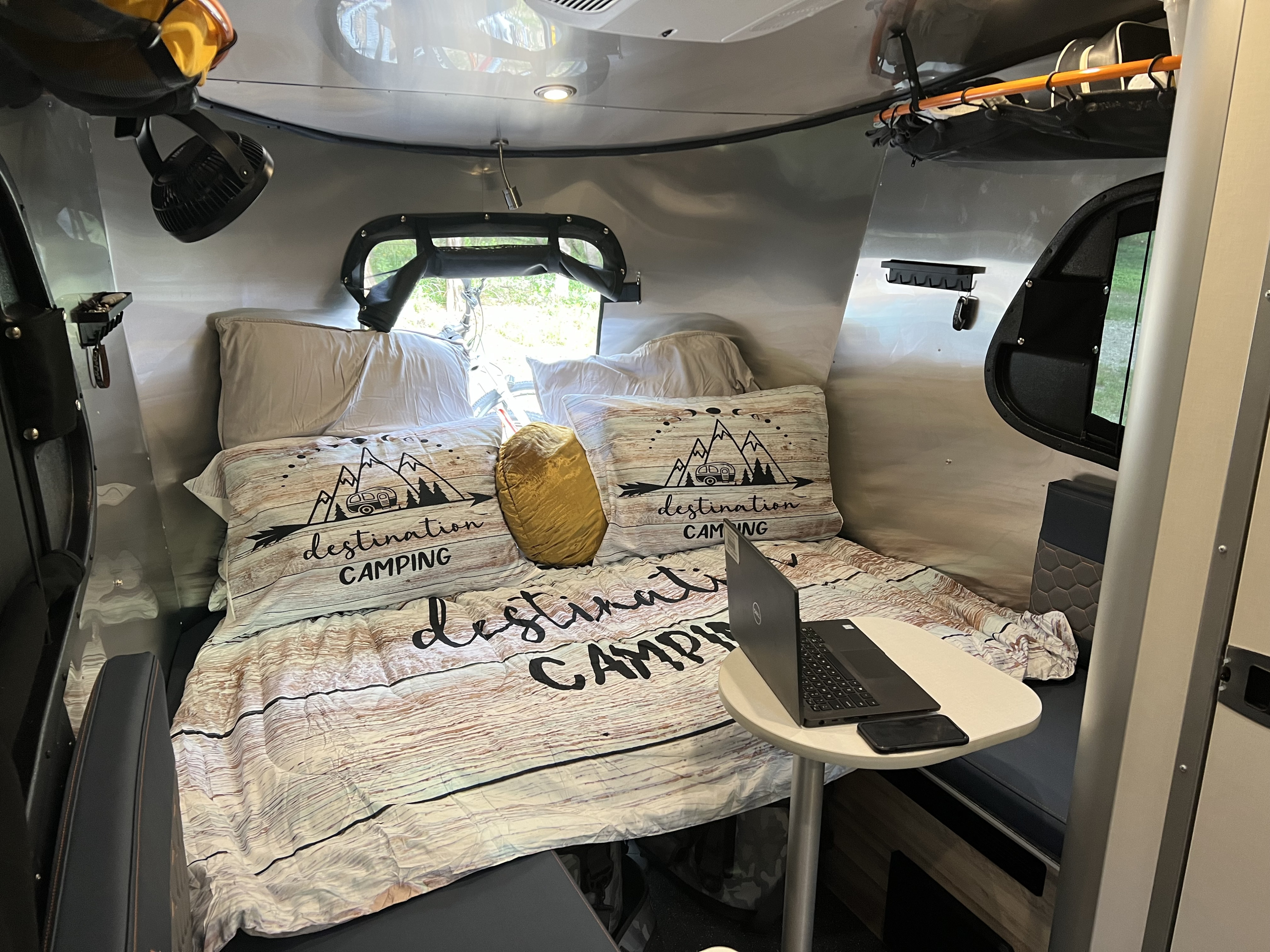 Cozy RV rental interior featuring a bed with "destination camping" bedding, laptop table, and ceiling fan.. Airstream Basecamp 2022