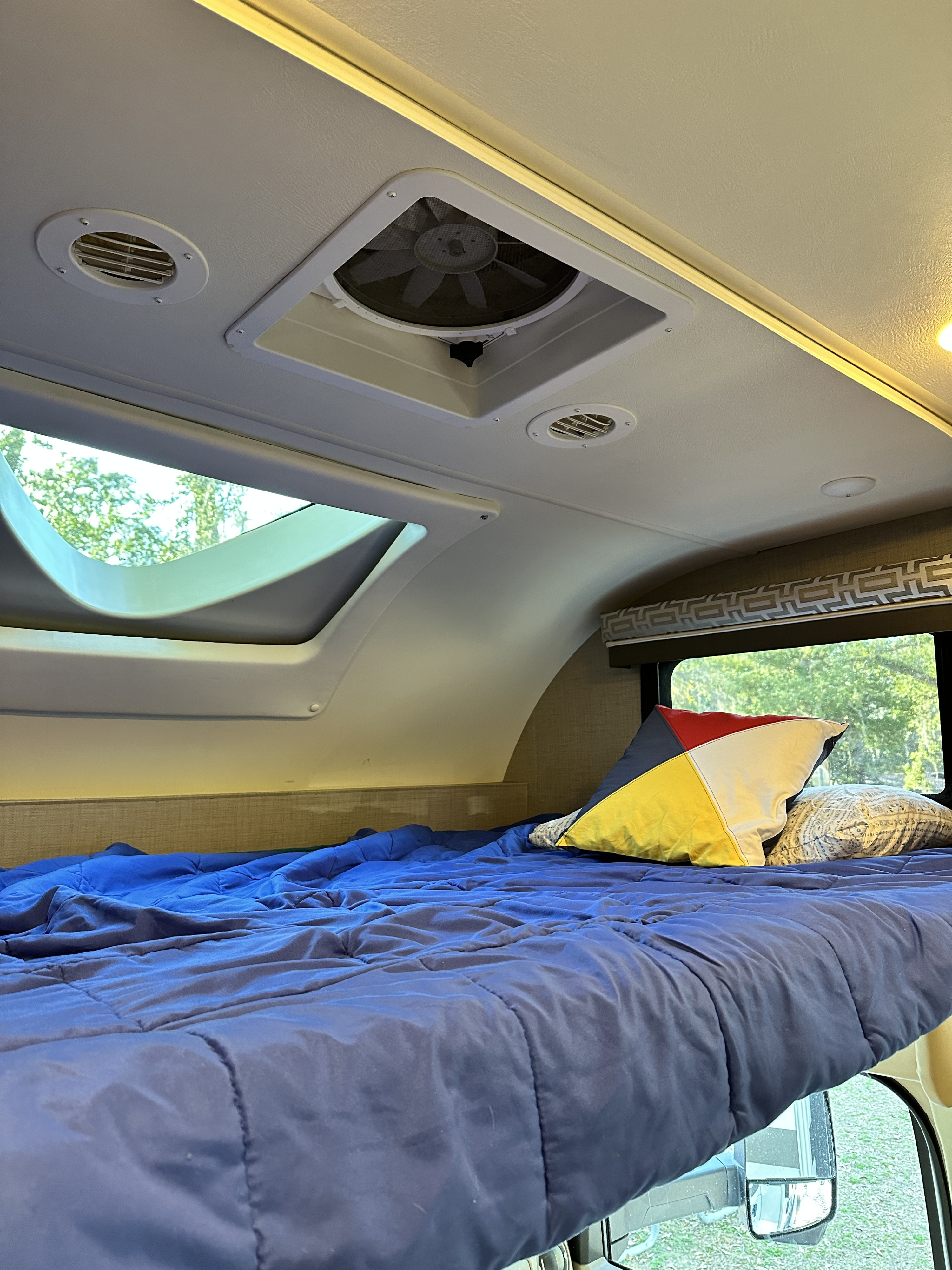 RV rental sleeping area: a comfortable bed with blue comforter, pillows, overhead skylight, fan, and vents.. Thor Quantum 2017
