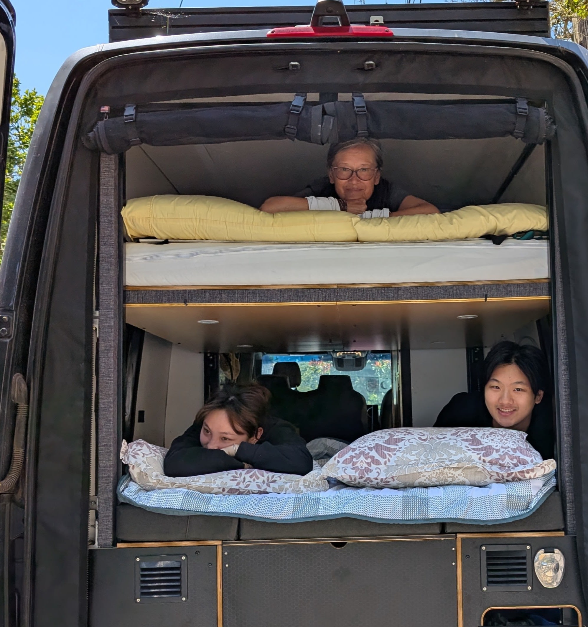 Family enjoying their RV rental: an older woman on the top bunk, two younger people below, peering out from the back.. Mercedes 4WD Sprinter 2500 (170 wheelbase) 2021