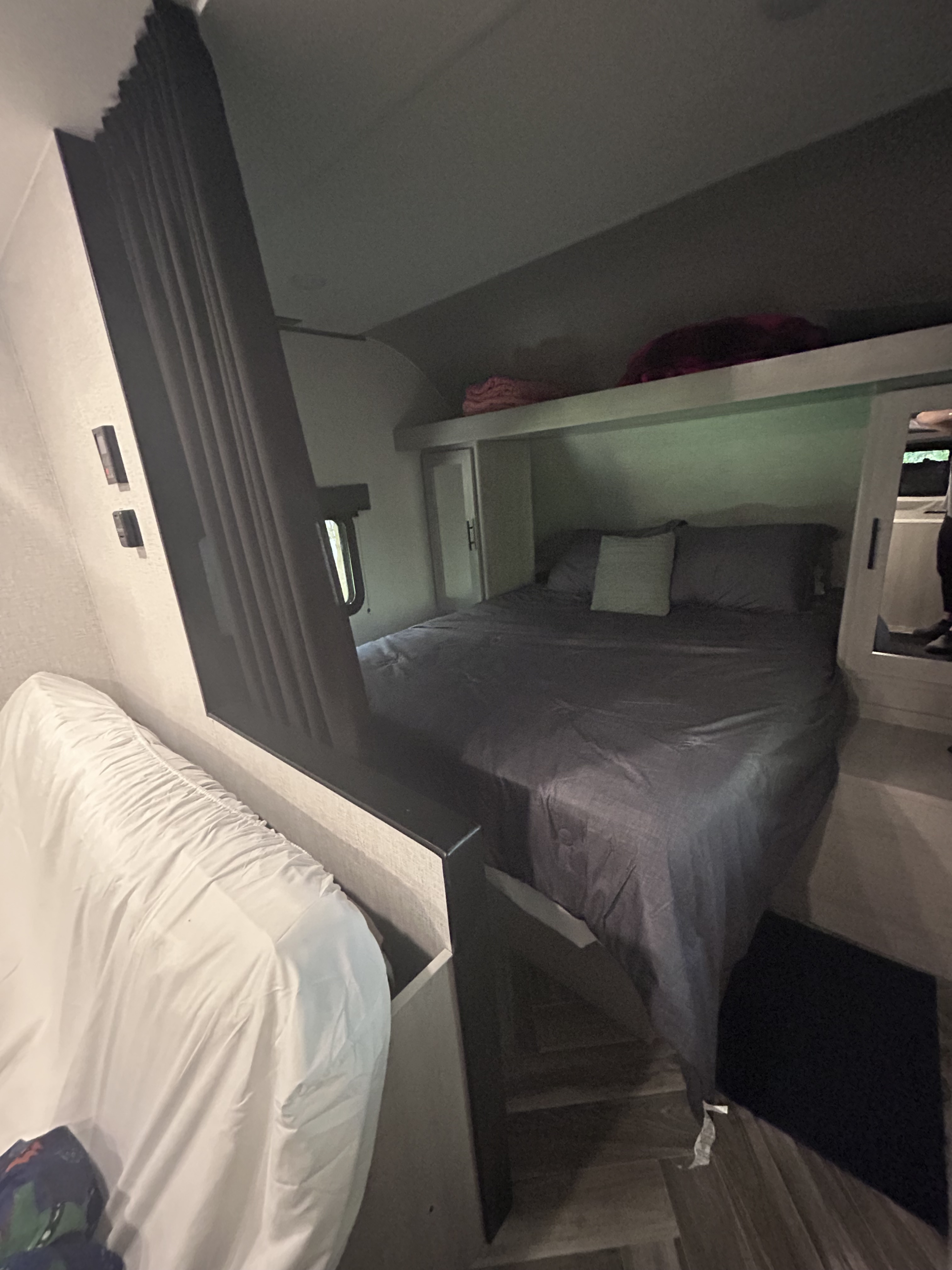Inside a cozy RV rental bedroom with a grey bed, overhead storage, and a white couch, ready for your next trip.. Crossroads Zinger Lite 2025