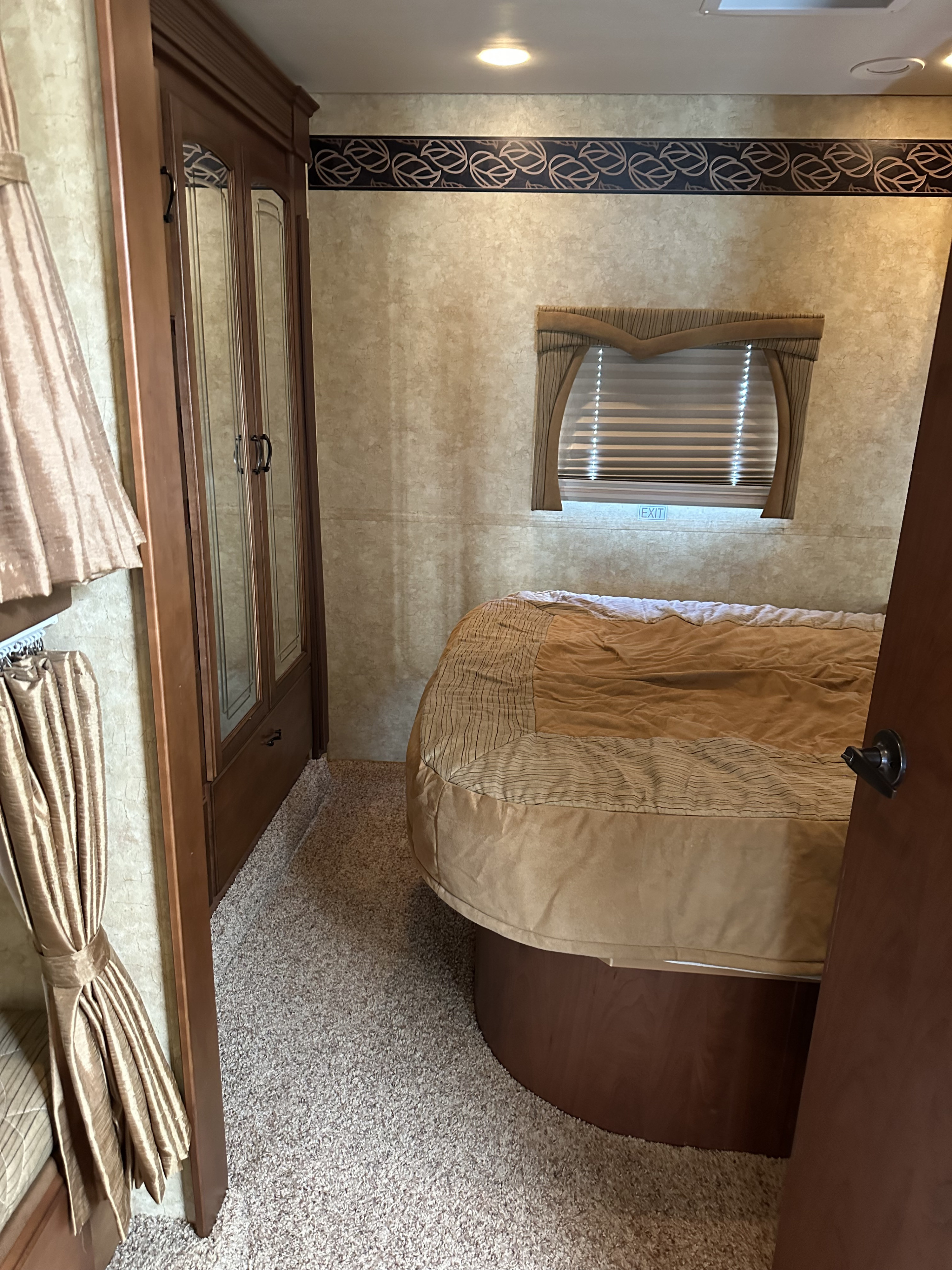 This cozy RV rental bedroom interior features a bed, wardrobe, and window with an 'EXIT' sign, offering comfort on the go.. Jayco Greyhawk 2011