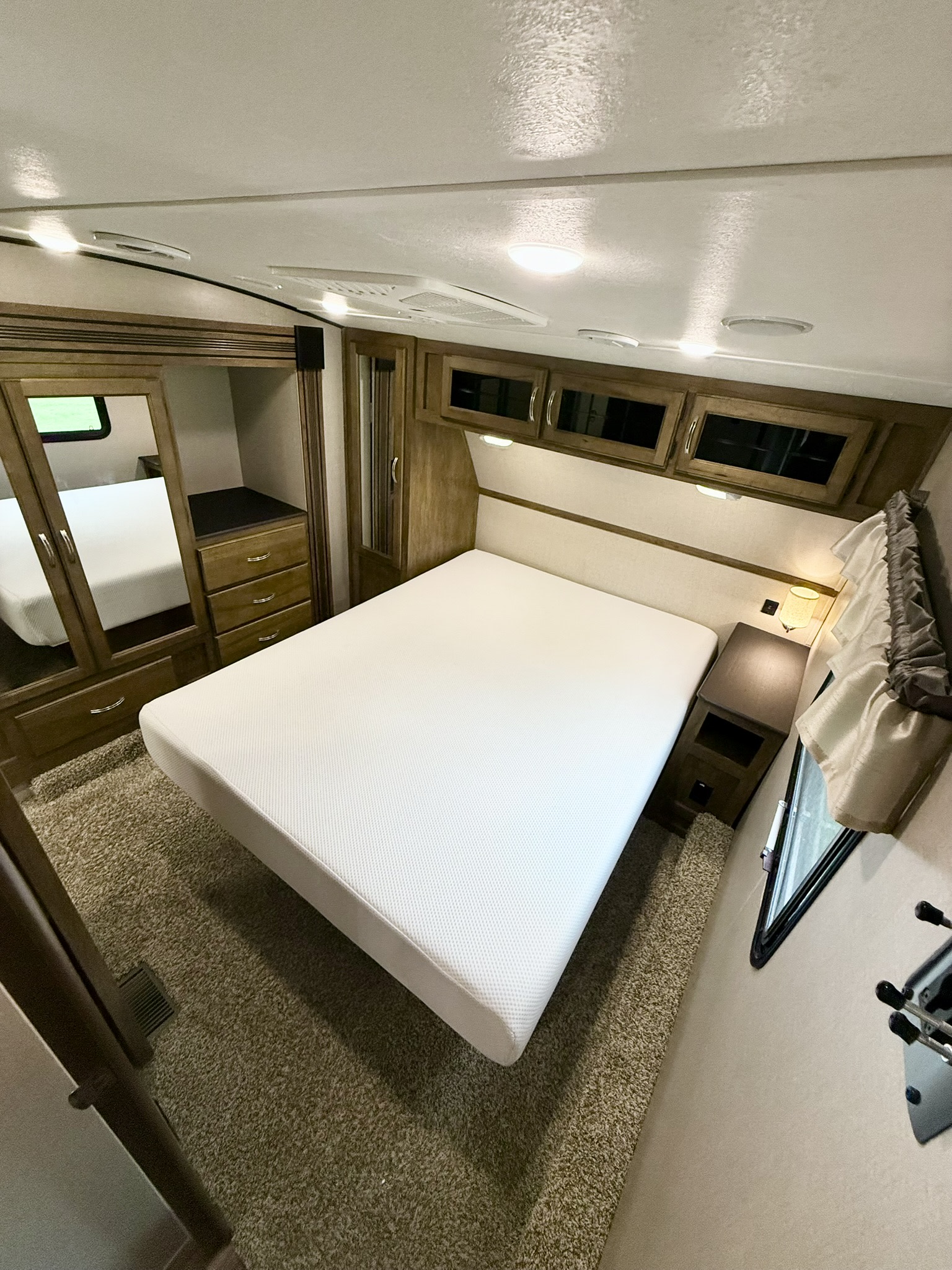 Spacious RV rental bedroom featuring a bed, wood cabinetry, a mirror, and soft lighting for cozy travel.. Coachmen Chaparral 2018
