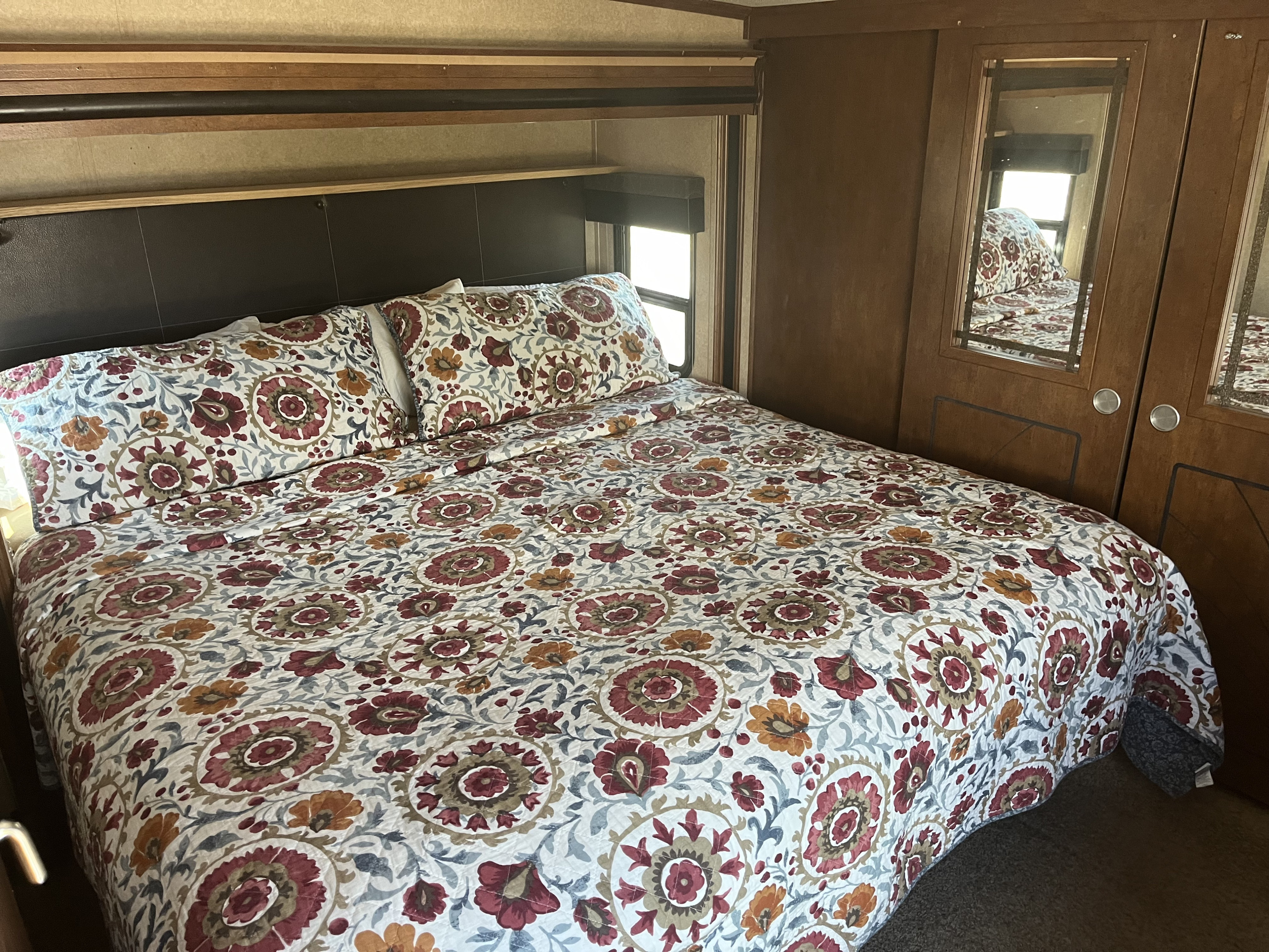 Cozy RV rental bedroom with floral comforter, built-in headboard, and mirrored wardrobe.. Forest River XLR Thunderbolt Toy Hauler 2014