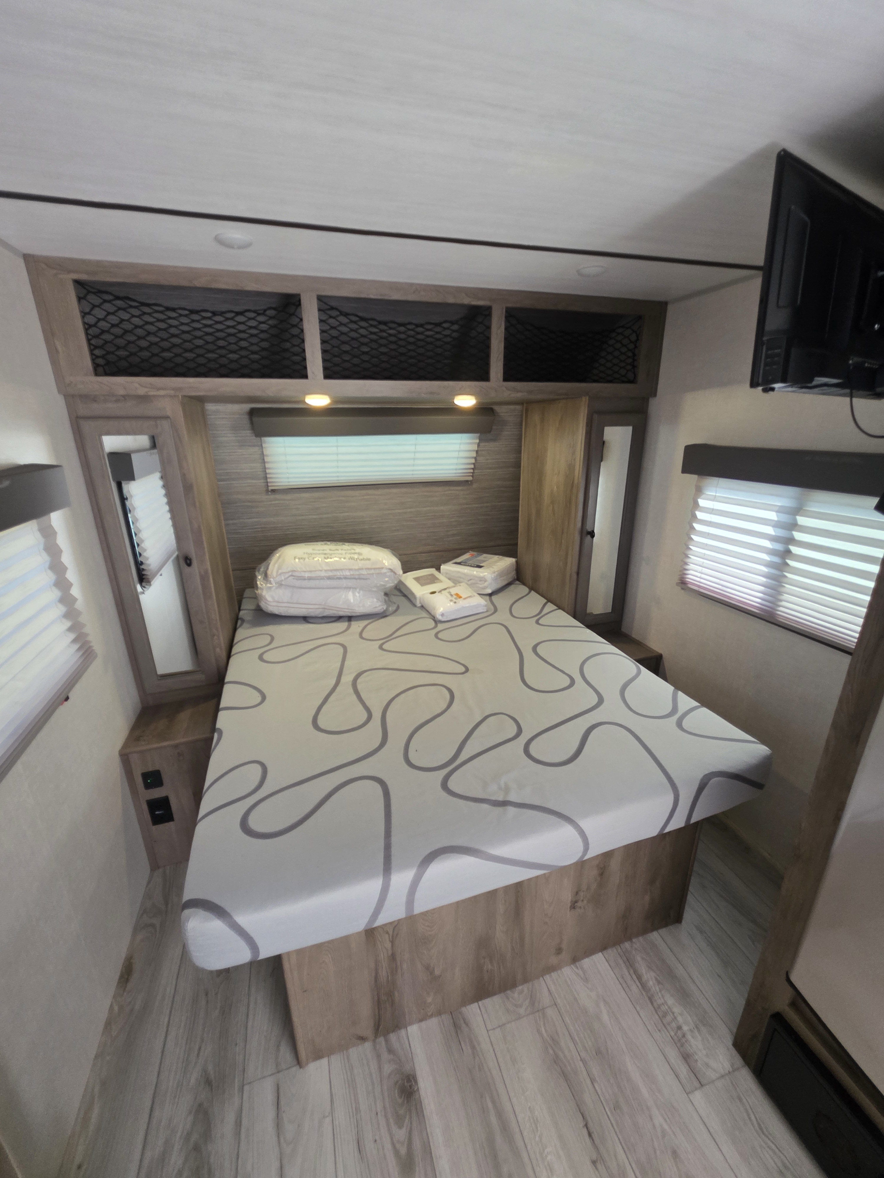 RV rental bedroom featuring a bed with new bedding, overhead storage, side windows, and a mounted TV.. Forest River Surveyor Legend 2022