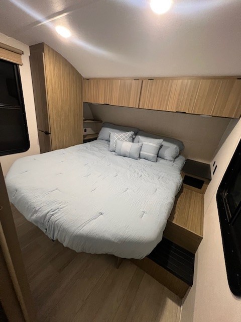 Inside an RV rental, this modern bedroom offers a light blue queen bed, built-in storage, and bright interior lighting.. Forest River 273QBXL 2025