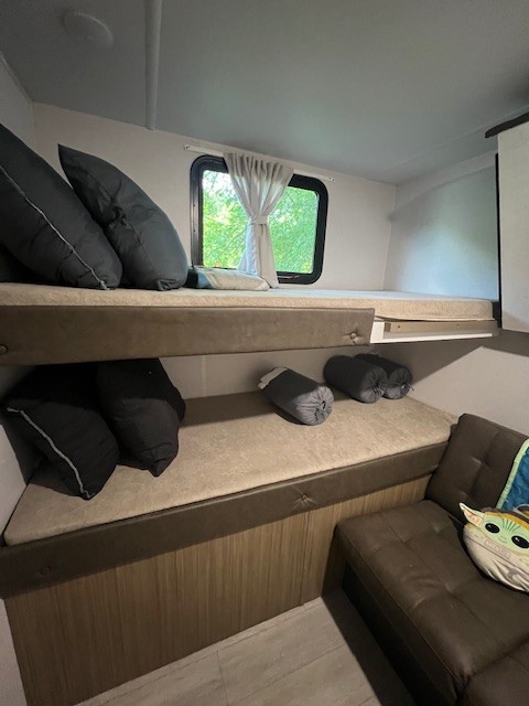 Inside an RV rental: a stacked bunk bed area with dark pillows, a bright window, and a lower lounge seat. Ideal for families.. Forest River 273QBXL 2025