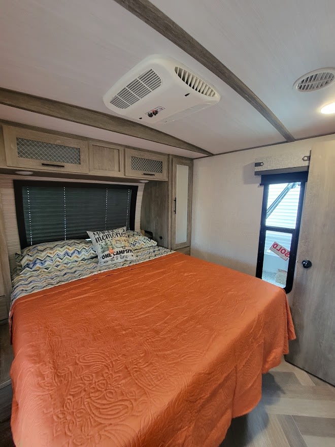 Cozy RV rental bedroom with a made bed, overhead cabinets, and AC for comfort. The window view includes a 'SOLD' sign.. Forest River Salem Hemisphere 2021