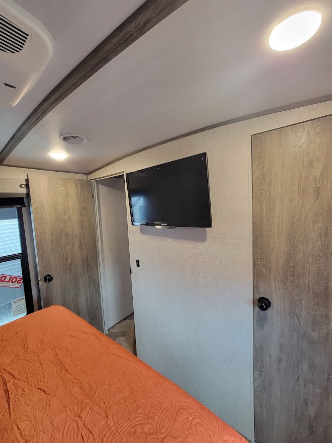Modern RV rental bedroom with an orange quilted bed, wall-mounted TV, and closet space for comfortable travel.. Forest River Salem Hemisphere 2021