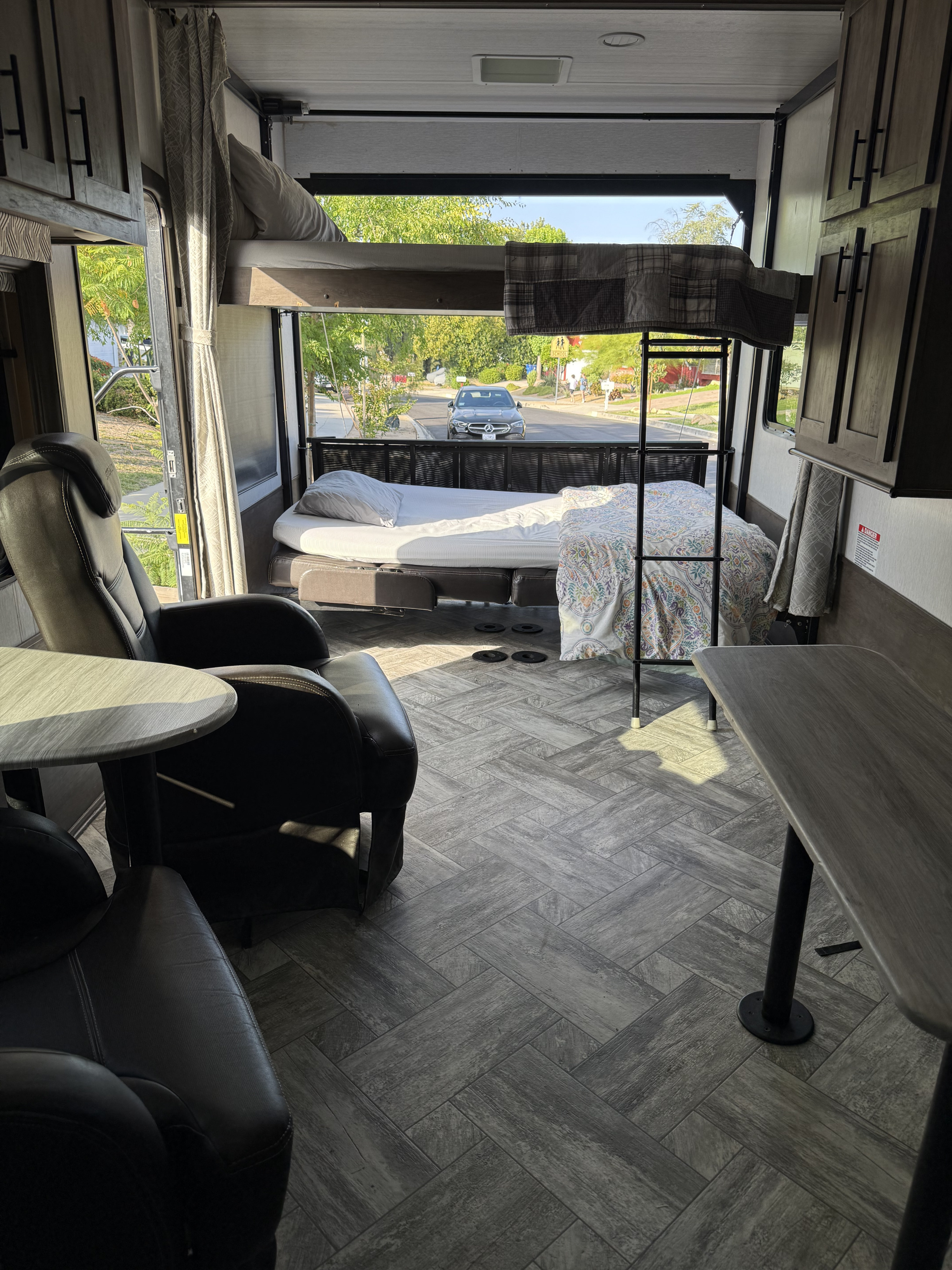 Spacious RV rental interior featuring bunk beds, recliners, and open rear ramp view of a sunlit street. Comfortable living.. Forest River Stealth 2022