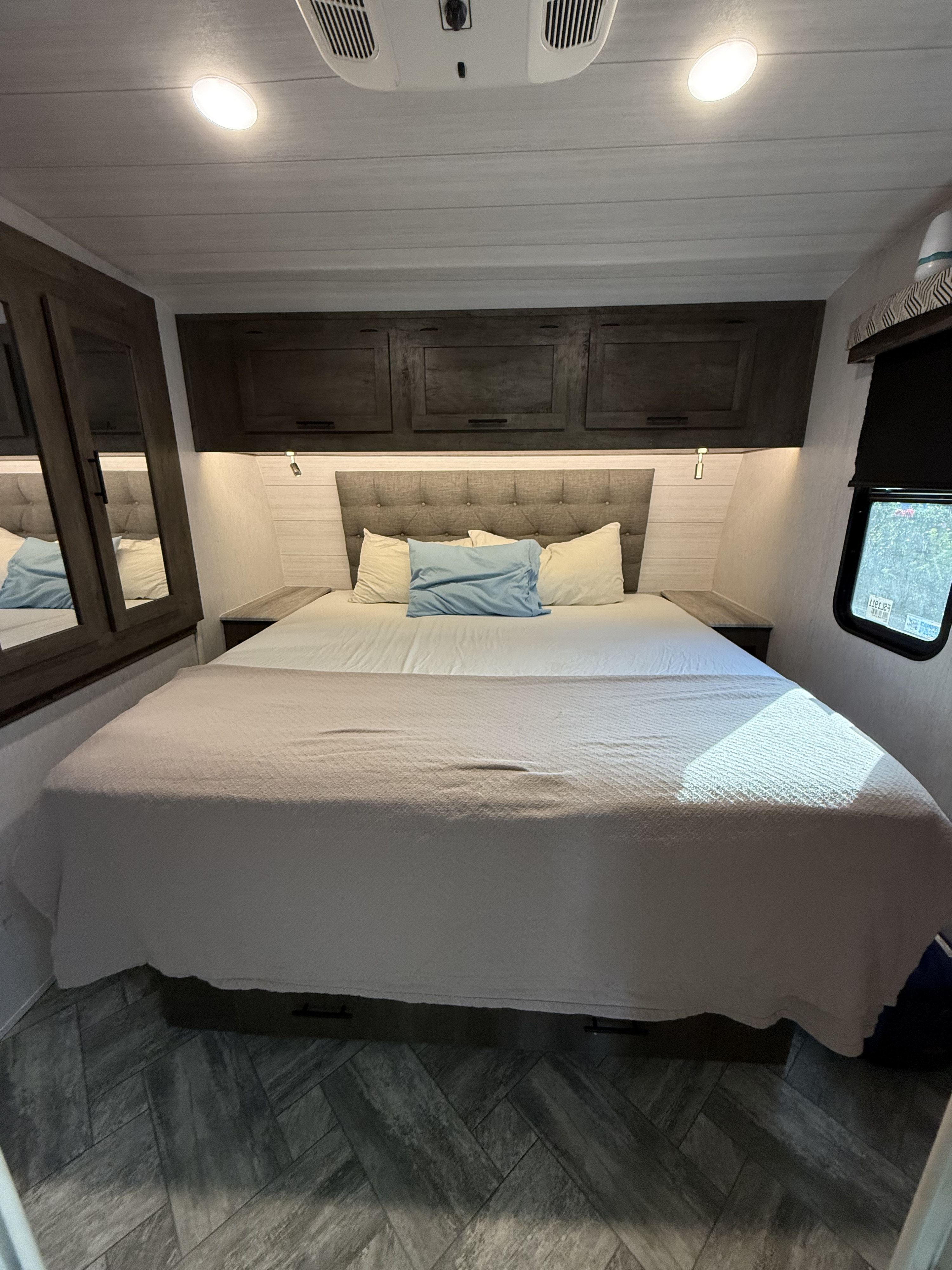 Cozy RV rental bedroom featuring a large bed with blue and white pillows, modern cabinets, and a stylish plank floor.. Forest River Stealth 2022