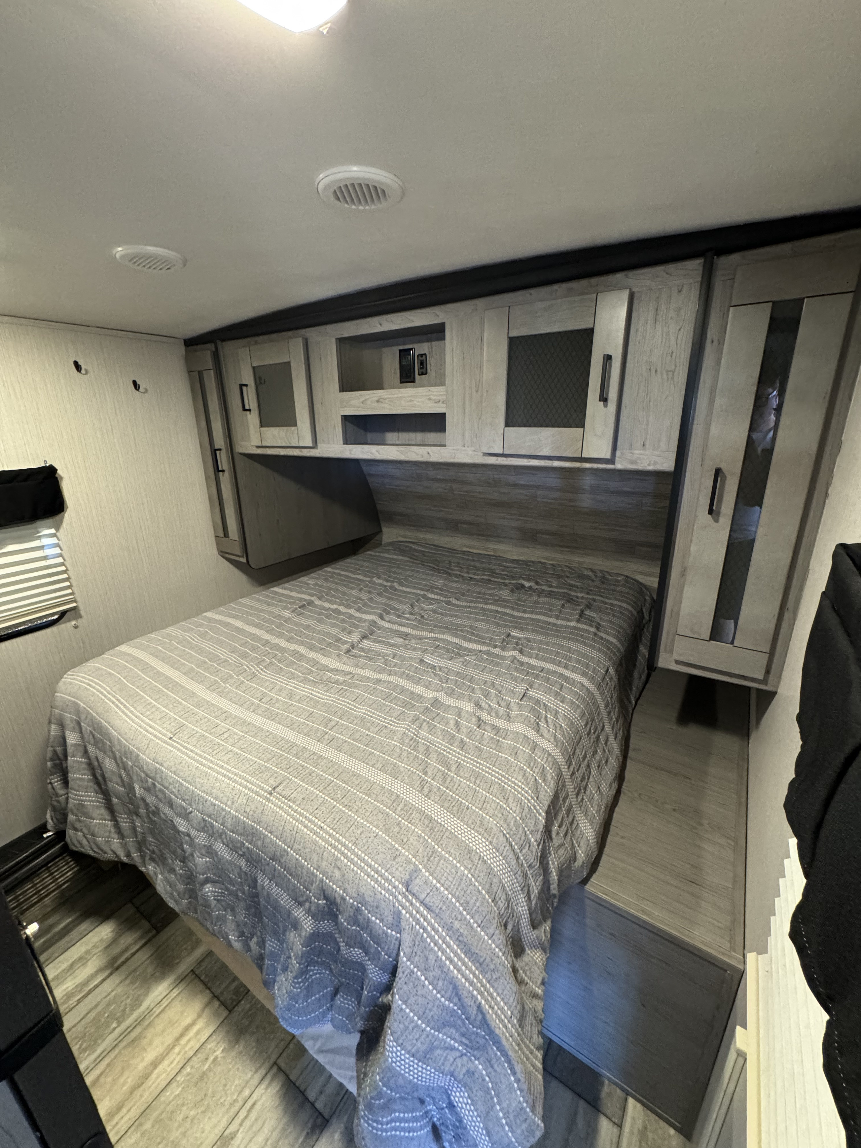 Cozy RV rental bedroom with a grey striped bed, overhead storage cabinets, and ceiling vents.. Heartland RVs North Trail 2021