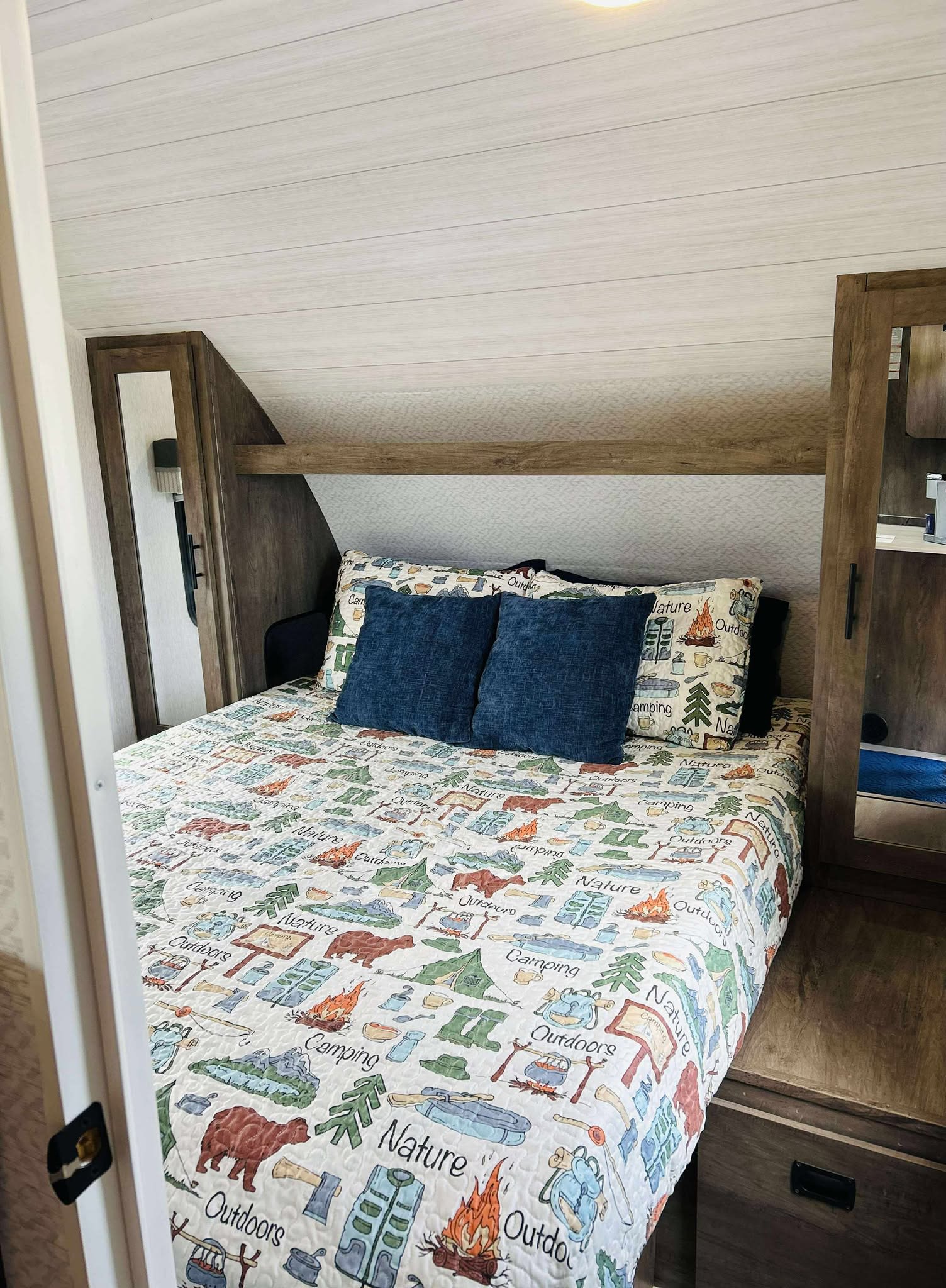 Inside an RV rental: a compact bedroom with a camping-themed bedspread, blue pillows, and wood cabinetry.. Forest River Salem Cruise Lite 2022