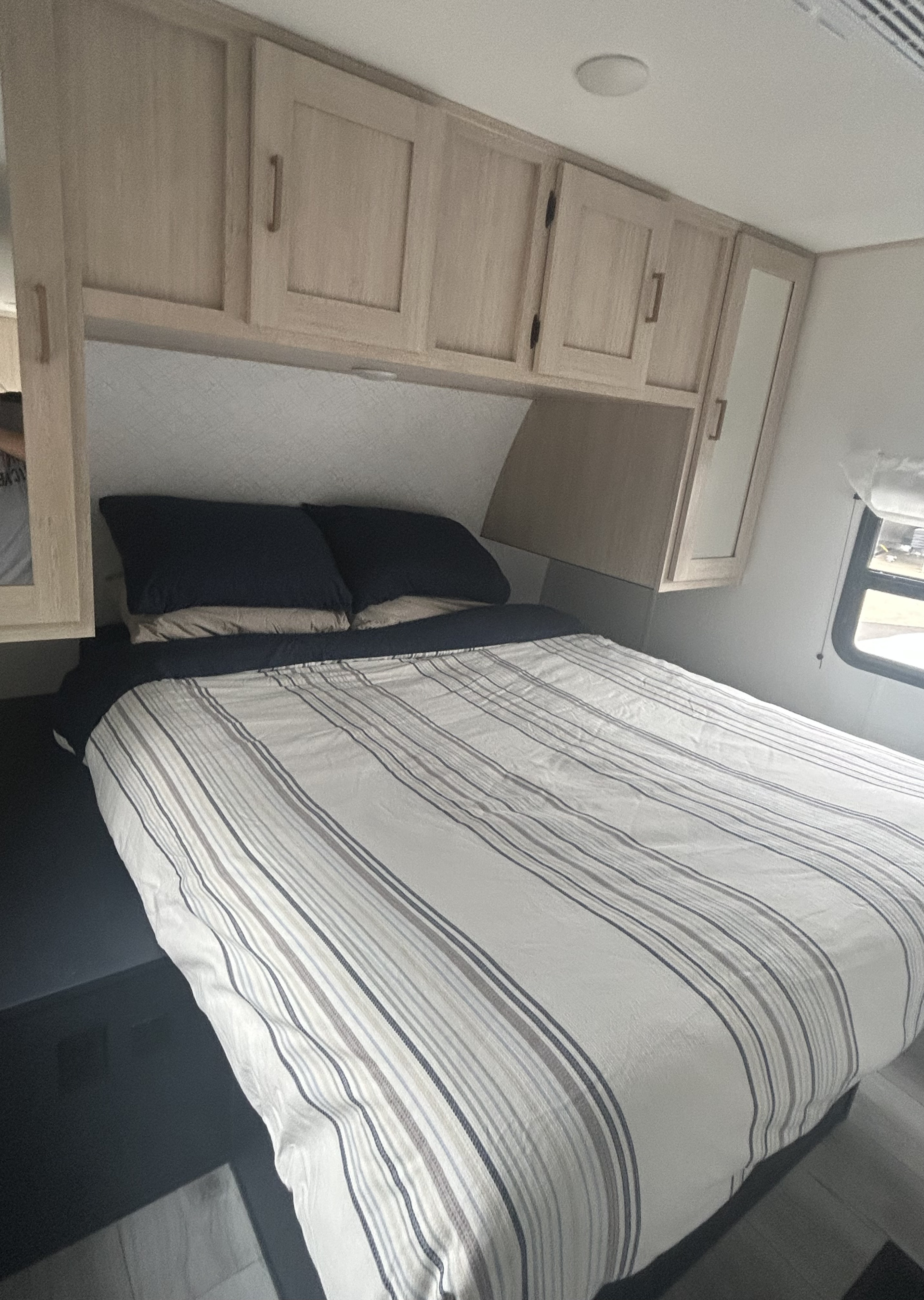 RV rental bedroom featuring a striped bed, dark pillows, and light wood overhead cabinets.. Forest River 2339176 2024