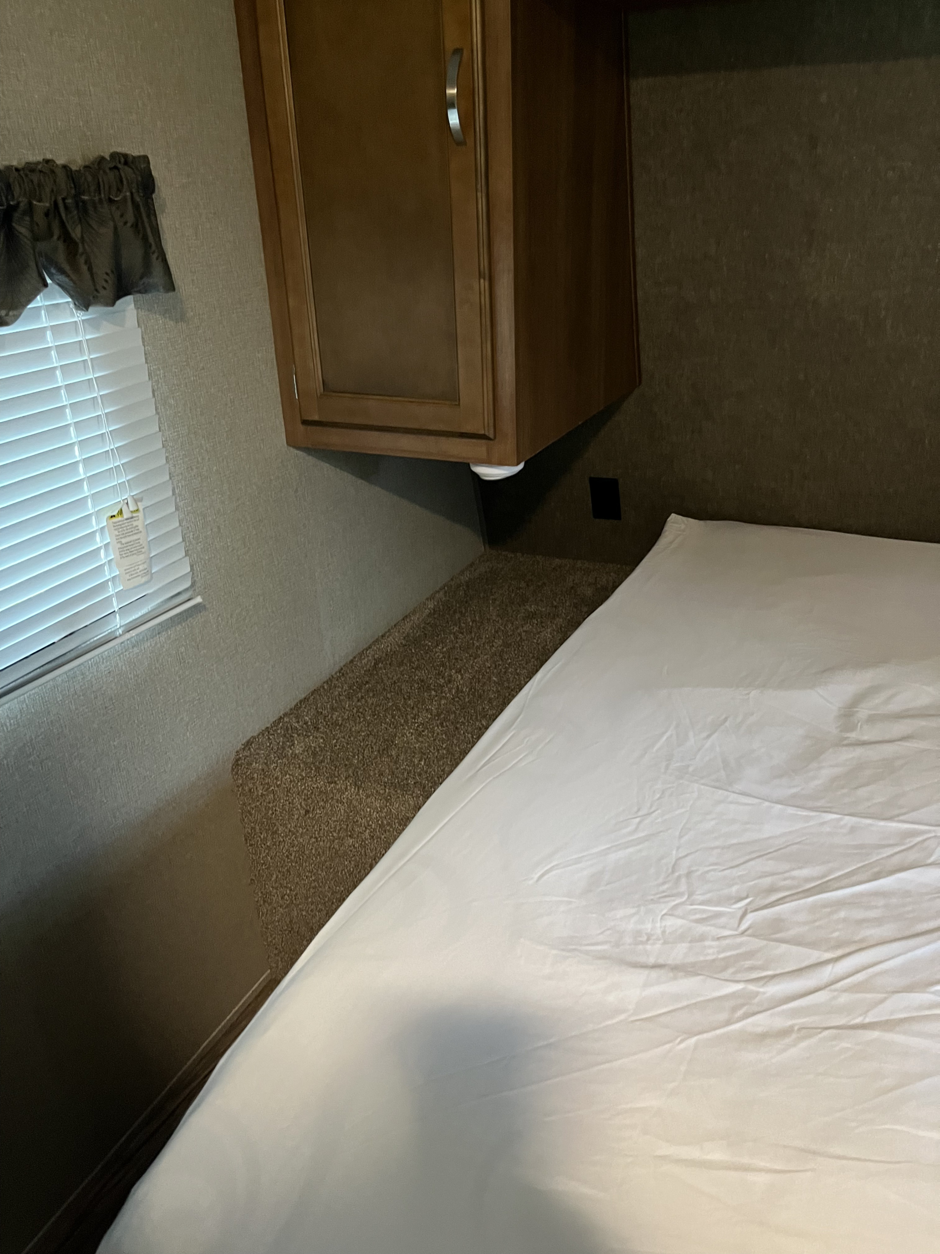 Inside an RV rental: a compact bedroom with a bed, wall-mounted cabinets, and a window with blinds.. Keystone RV Springdale 2019