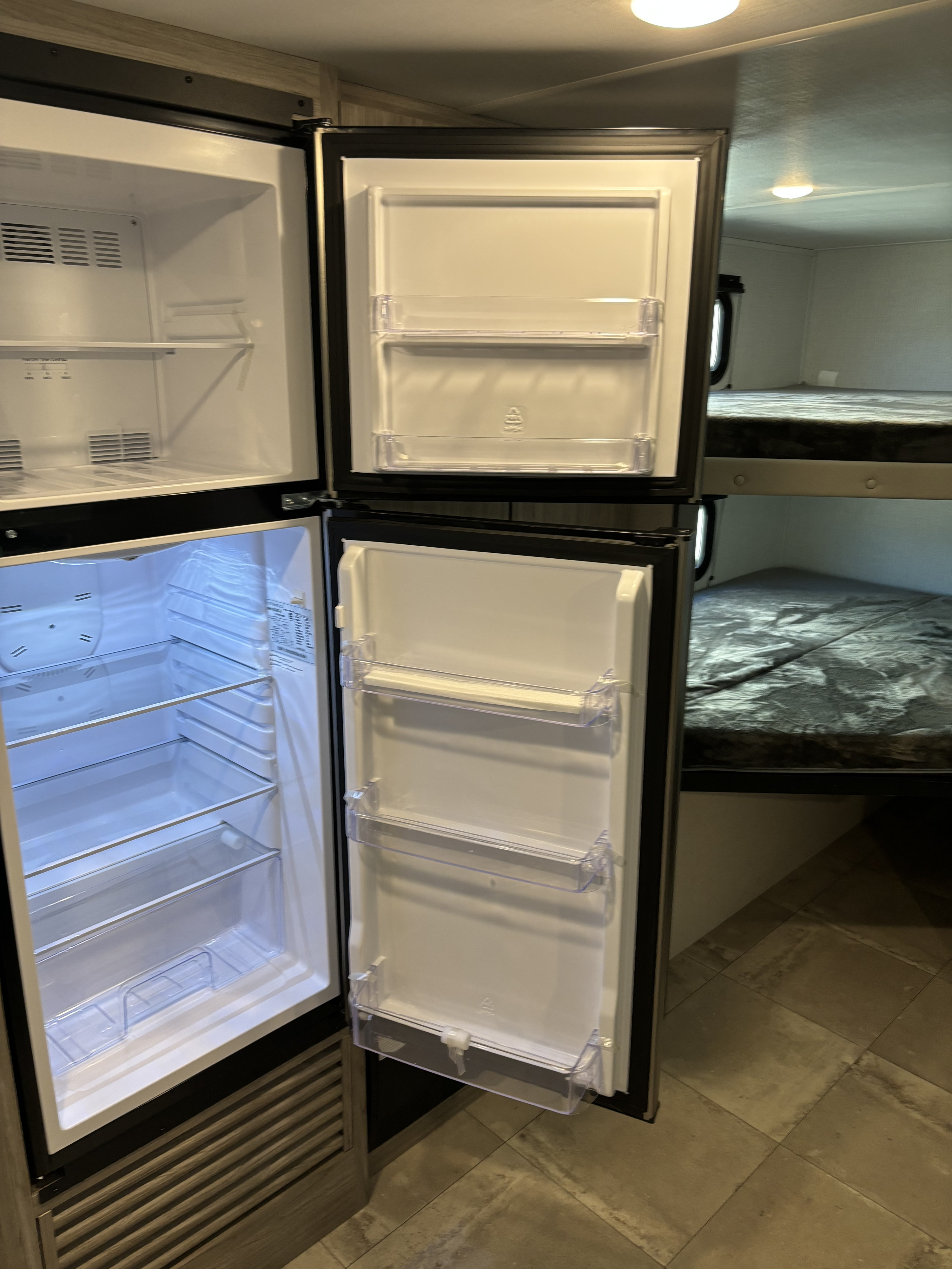 Spacious RV rental interior with an open fridge/freezer, empty shelves, and cozy bunk beds.. Keystone RV Passport SL Ultra Lite 2024