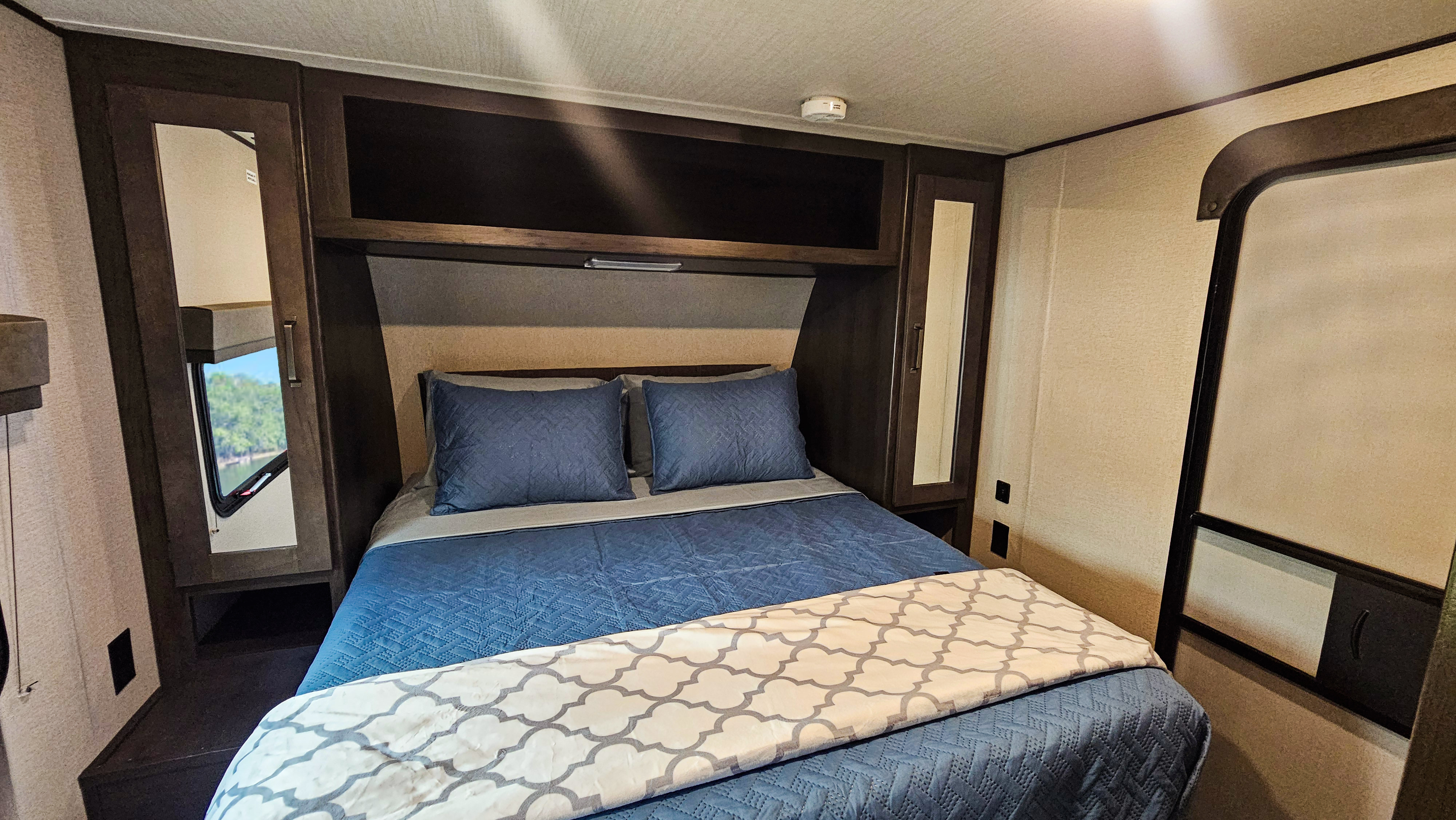 Cozy RV rental bedroom featuring a queen bed with blue bedding, built-in storage, and mirrored closets for your travels.. Grand Design Transcend Xplor 2022
