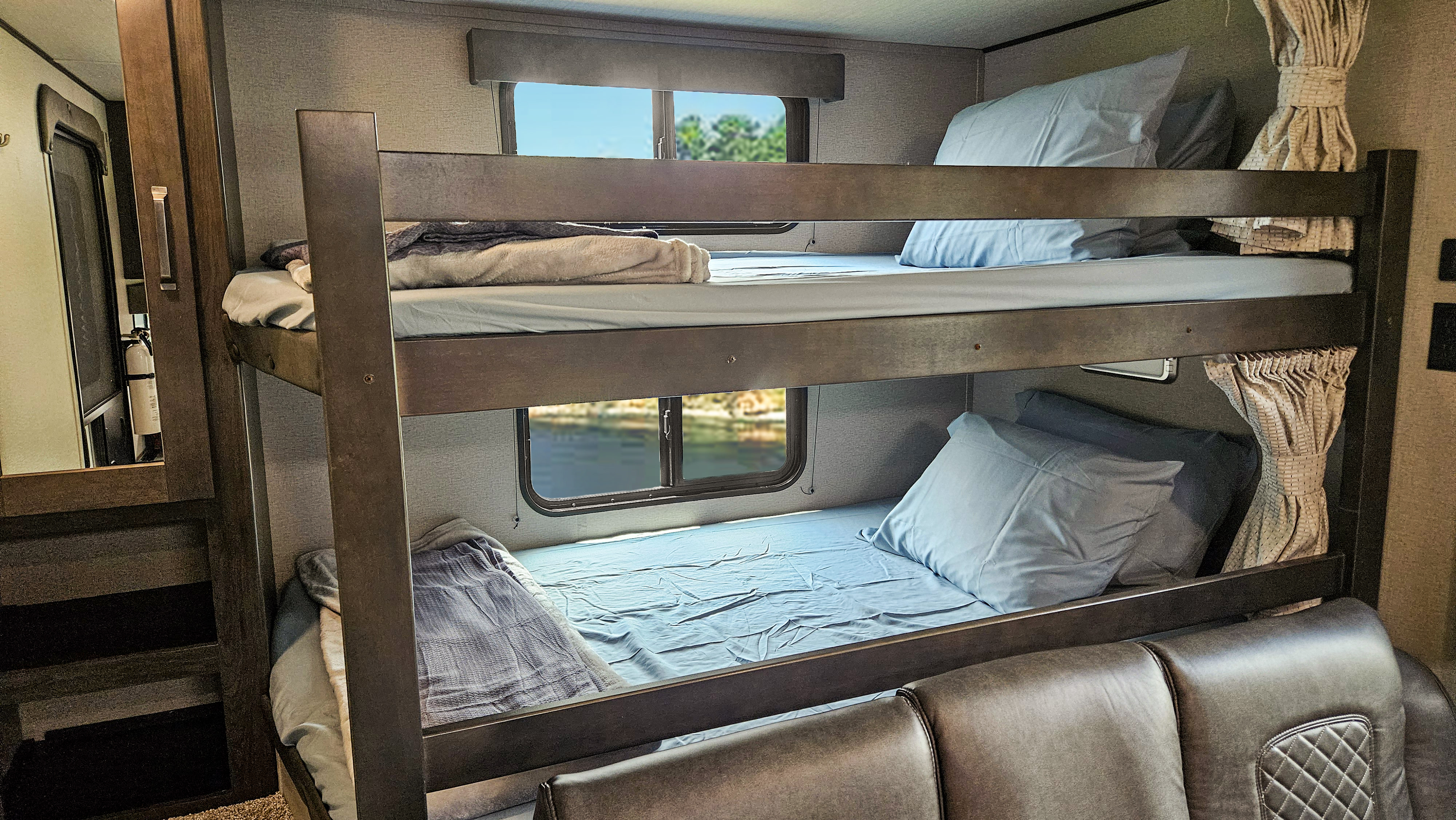 This RV rental features comfortable bunk beds with light blue bedding, scenic window views, and a fire extinguisher.. Grand Design Transcend Xplor 2022