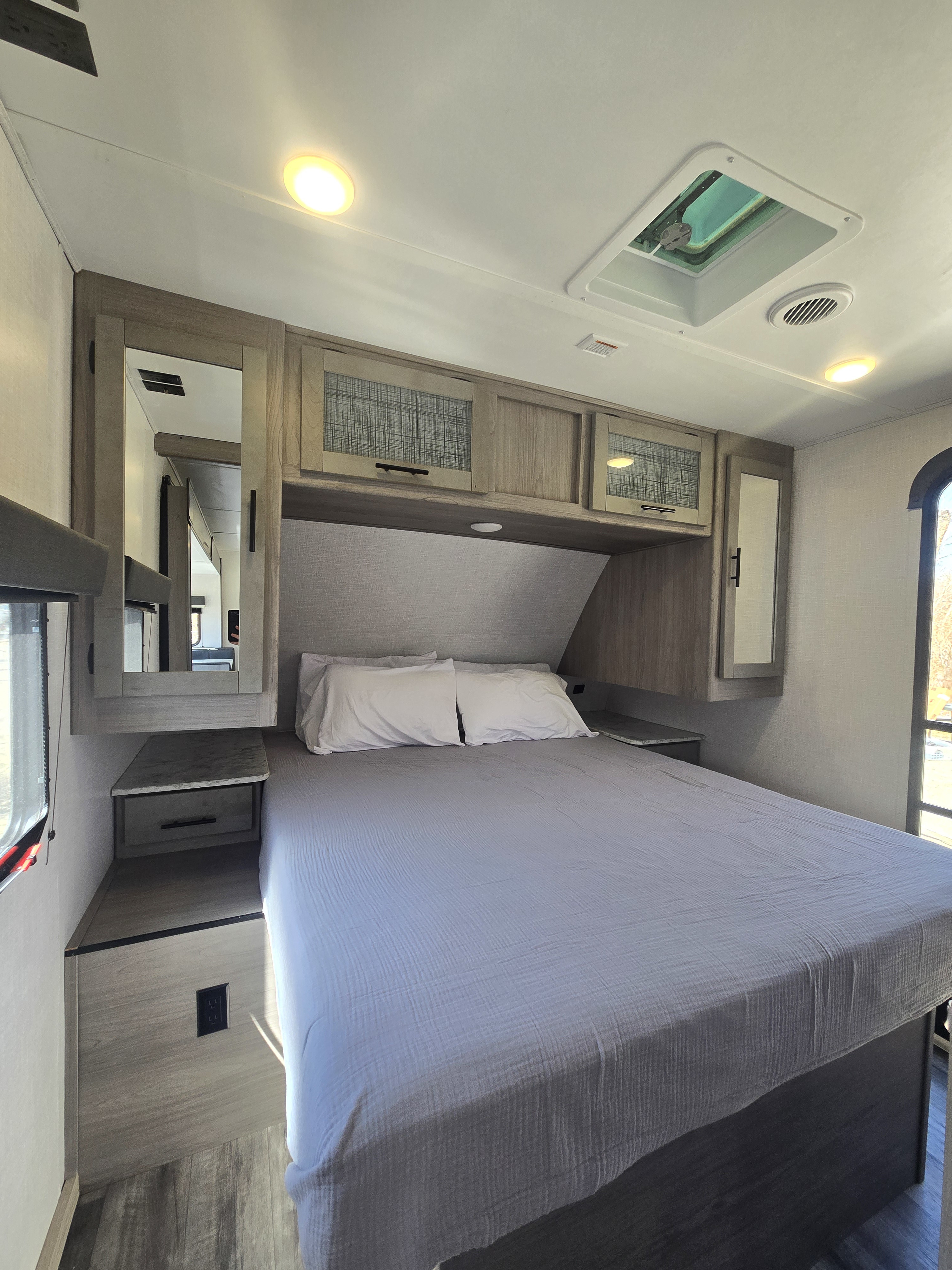 Cozy RV rental bedroom featuring a large bed, overhead storage, integrated mirrors, and a ceiling vent.. Coleman Lite Series 2755BH 2022