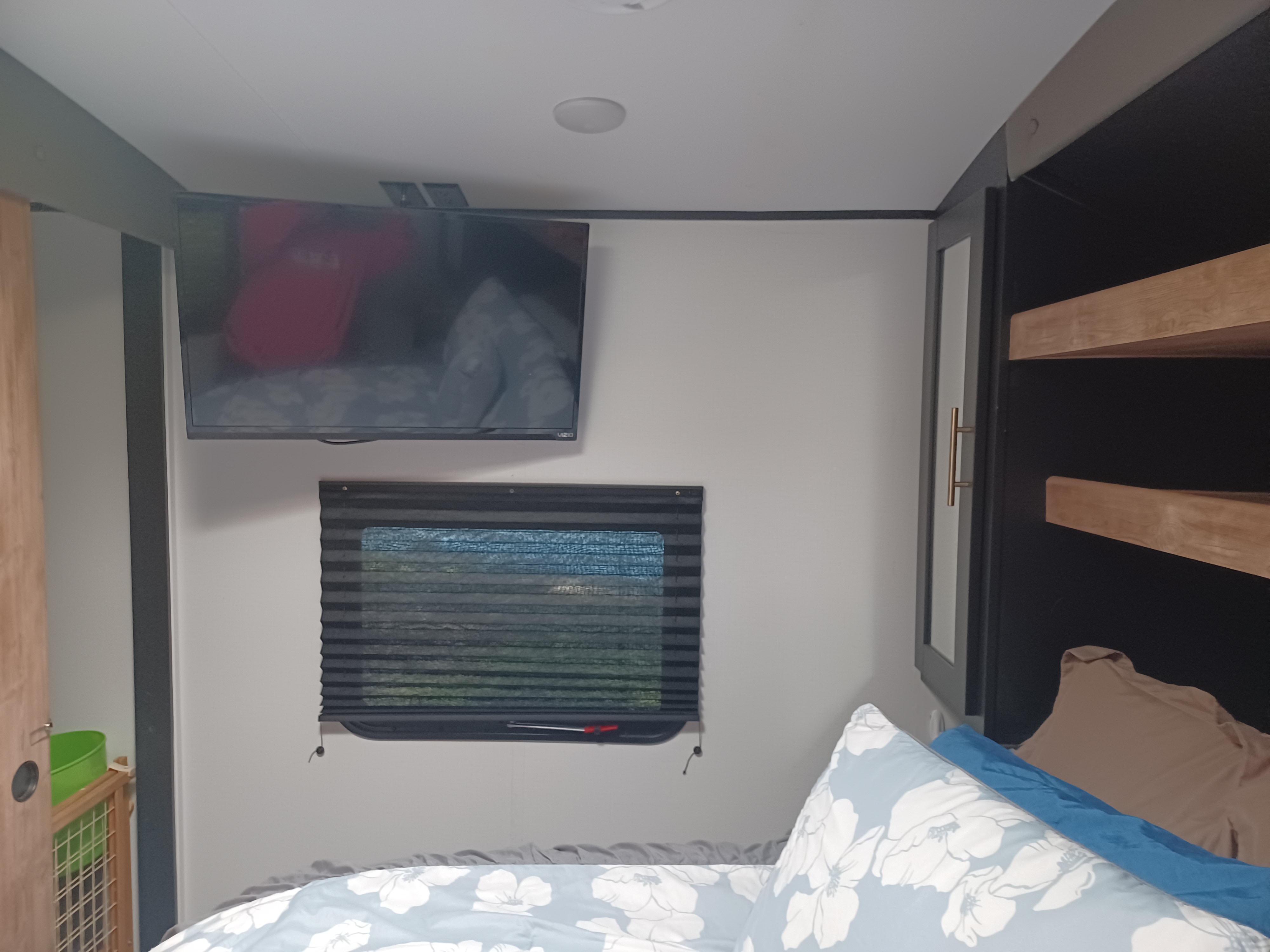 RV rental bedroom featuring a mounted TV, a window with pleated blinds, and practical storage shelving above a comfortable bed.. Keystone RV Springdale 2022