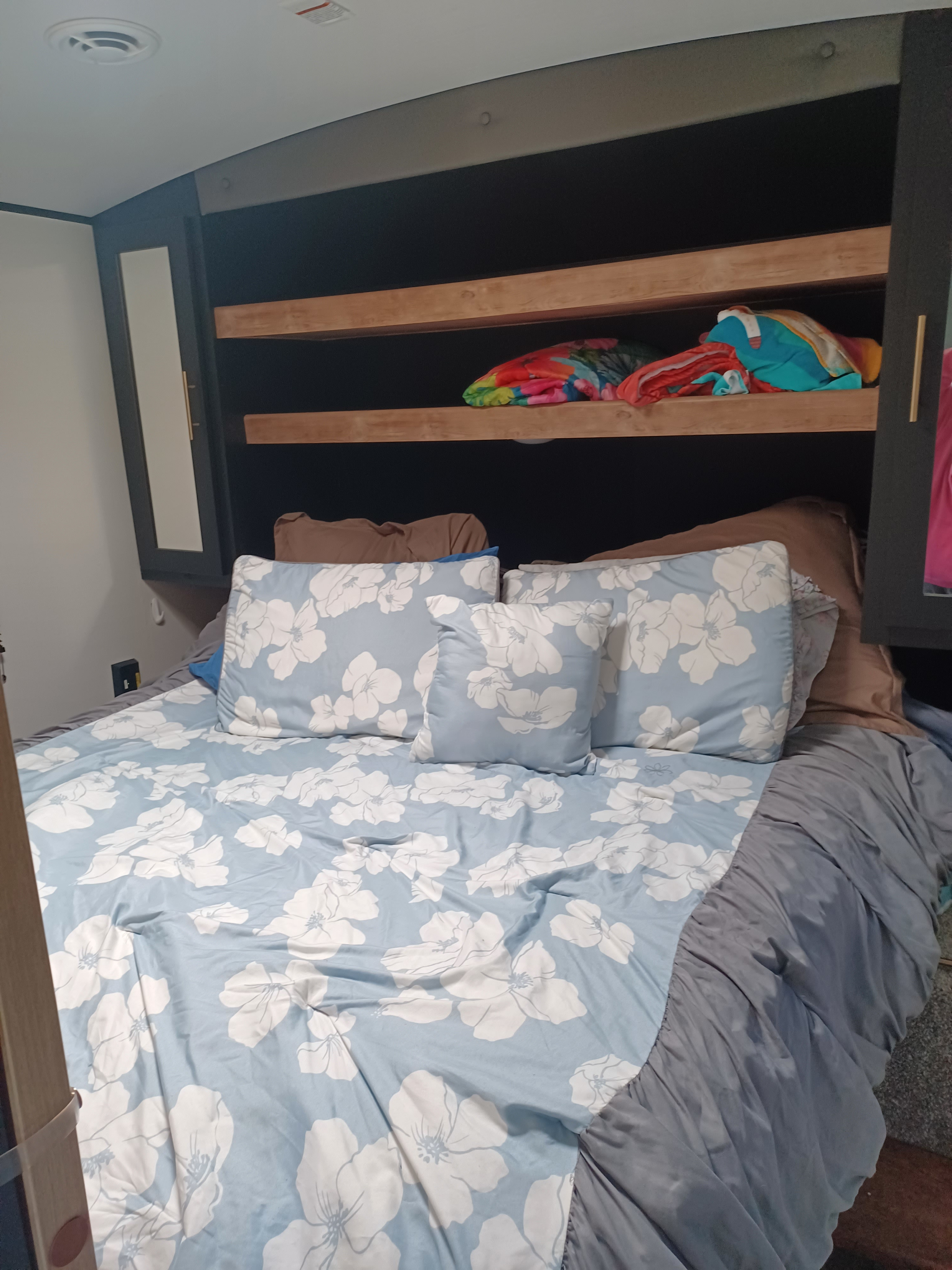 Experience a comfortable RV rental stay in this bedroom featuring a floral bed, built-in headboard with storage shelves & cabinets.. Keystone RV Springdale 2022