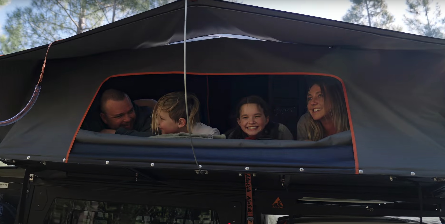 A happy family peers from a dark gray rooftop tent, likely part of their RV rental adventure. Smiles abound!. Chevrolet colorado 2025