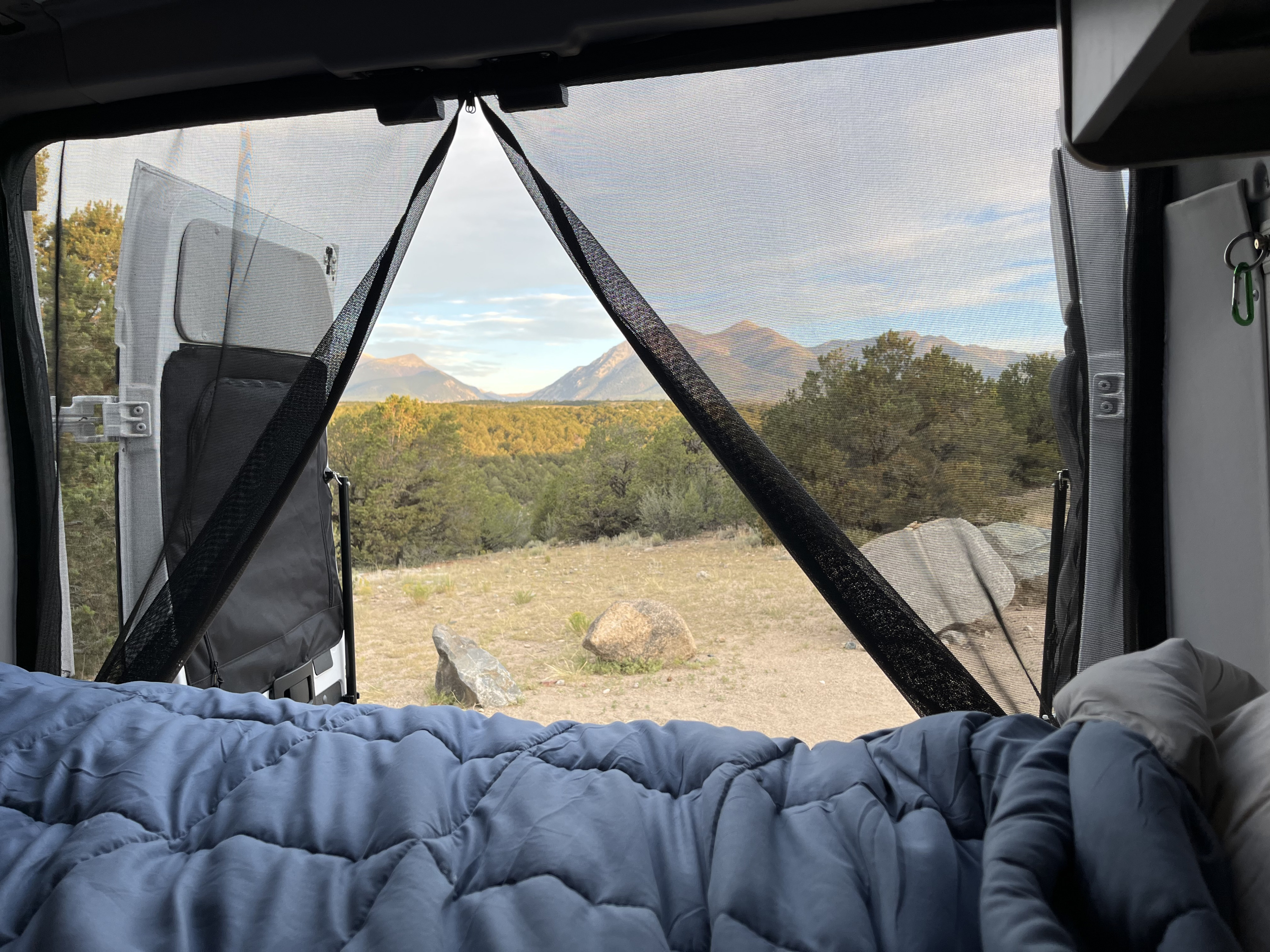Cozy RV rental bed view through bug screens to majestic mountains and serene forest. Perfect for outdoor escape.. Winnebago Solis 2021