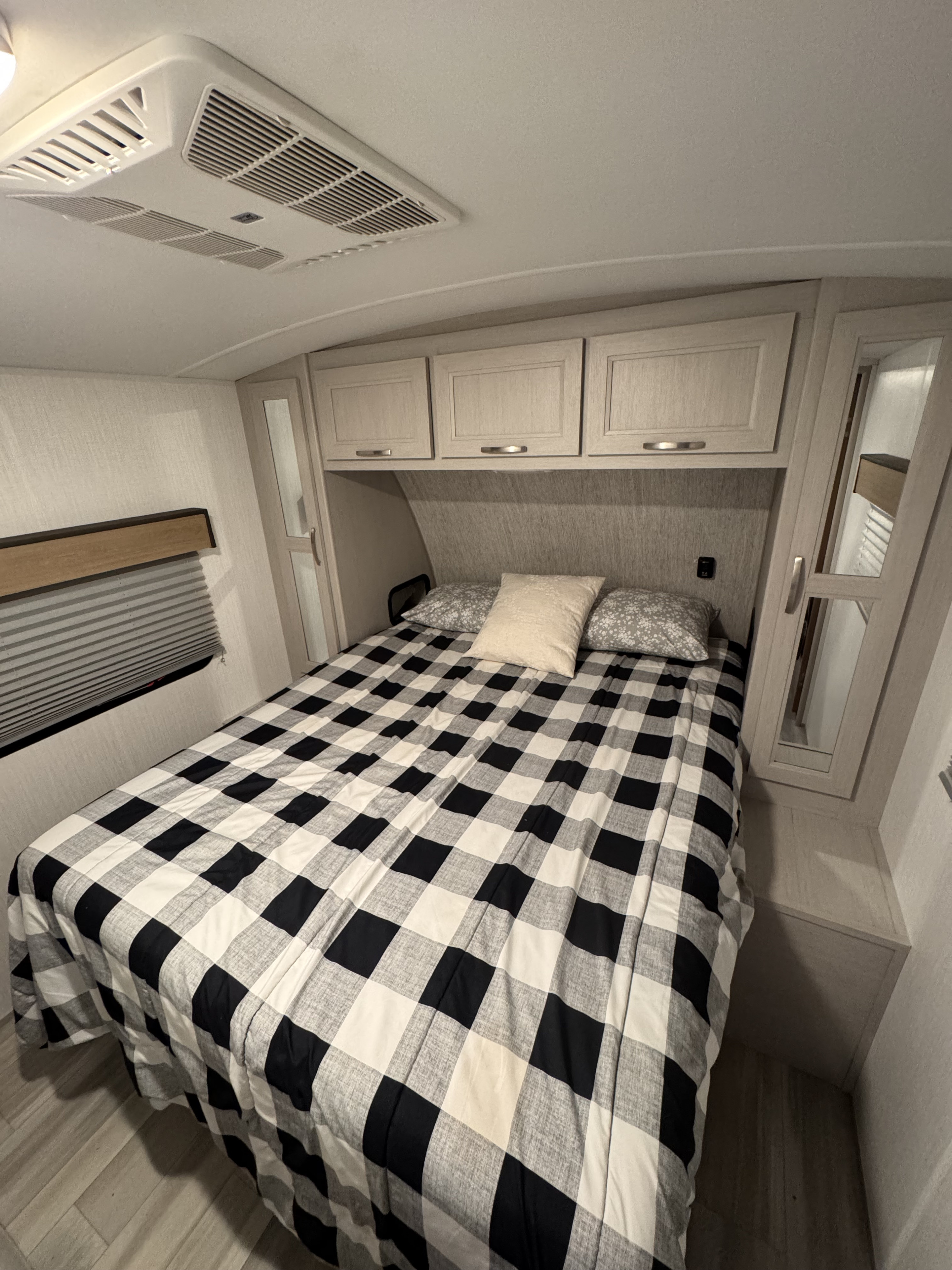 Comfortable RV rental bedroom: black & white checkered bed, overhead AC, storage cabinets, and blinds. Ready for travel.. Cruiser RV Embrace 2024