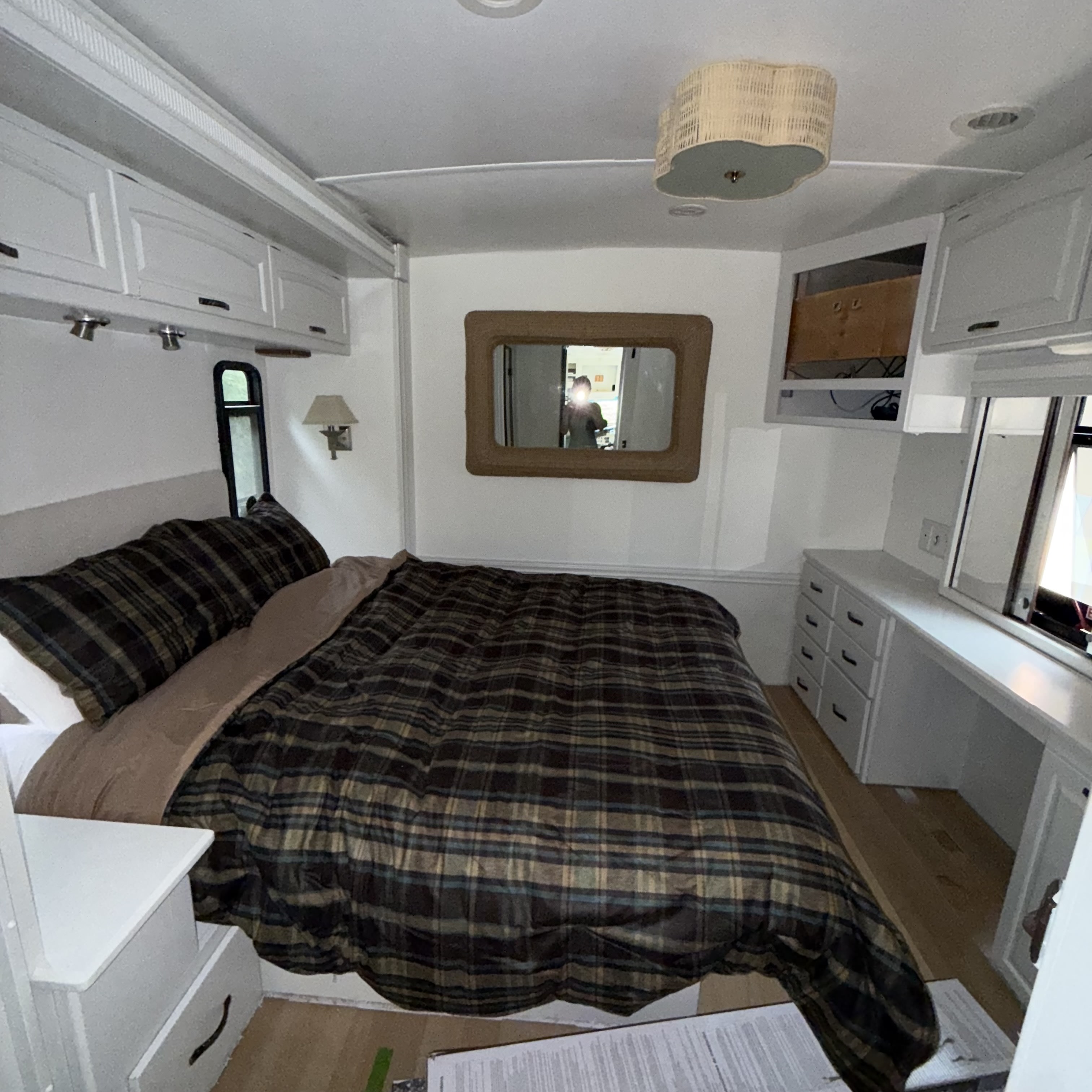 Comfortable RV rental bedroom interior with a large bed, plaid bedding, white overhead cabinets, and built-in vanity storage.. Itasca Suncruiser 2006