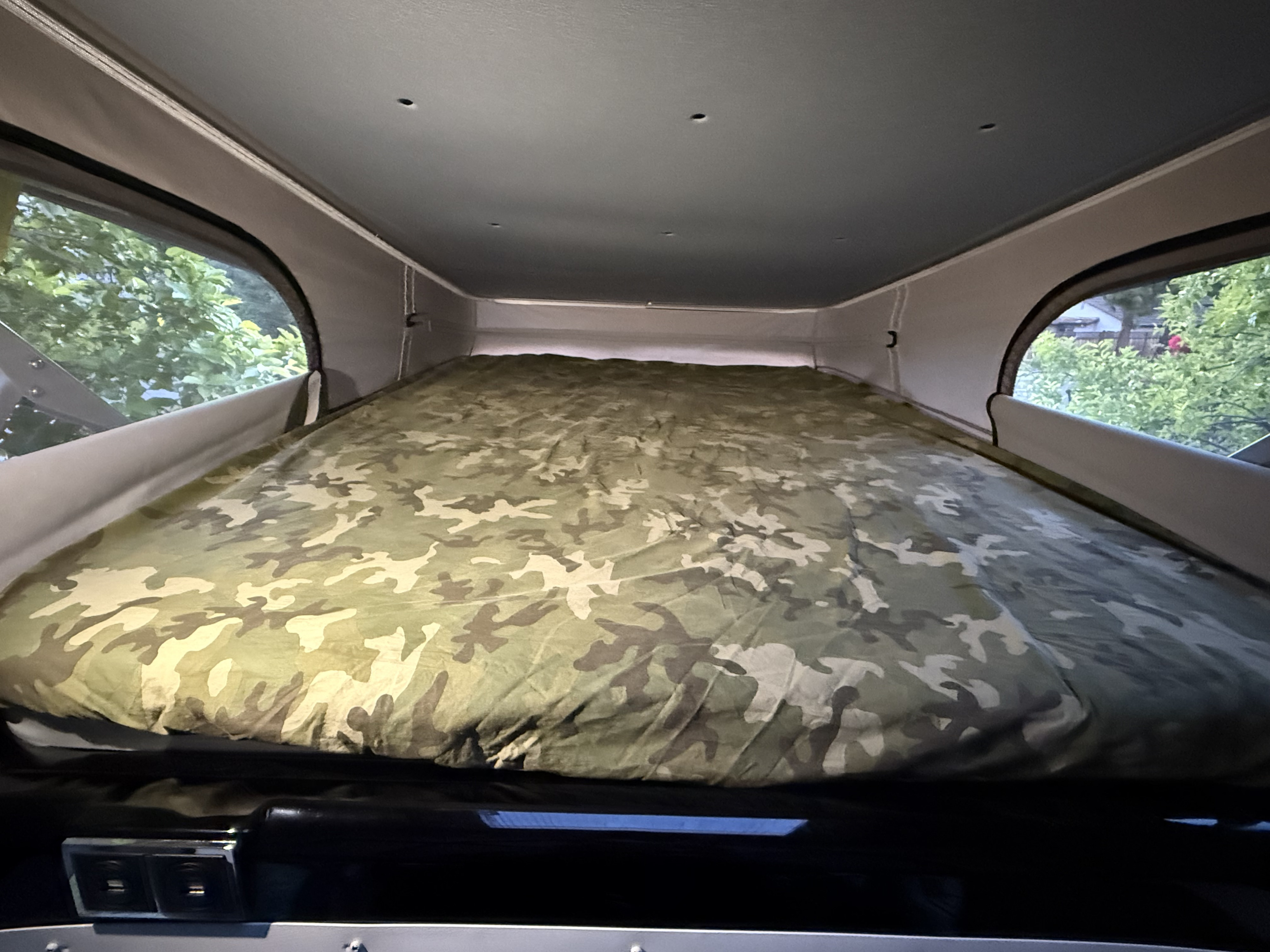 Cozy camo bed inside an RV rental pop-top camper, offering a peaceful view of nature from the windows. Perfect for camping.. Thor Motor Coach Sequence 2022