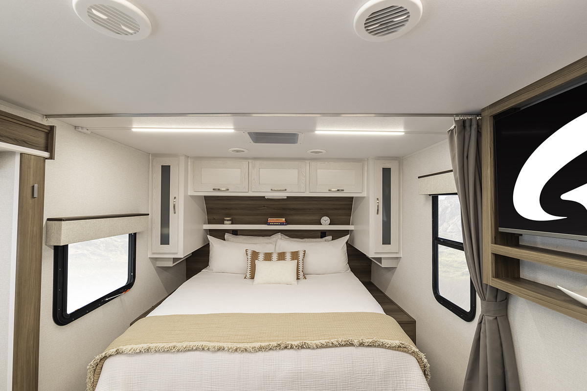 Cozy RV rental bedroom with queen bed, overhead cabinets, windows, and TV, perfect for comfortable travel.. Go Explore X203 2025